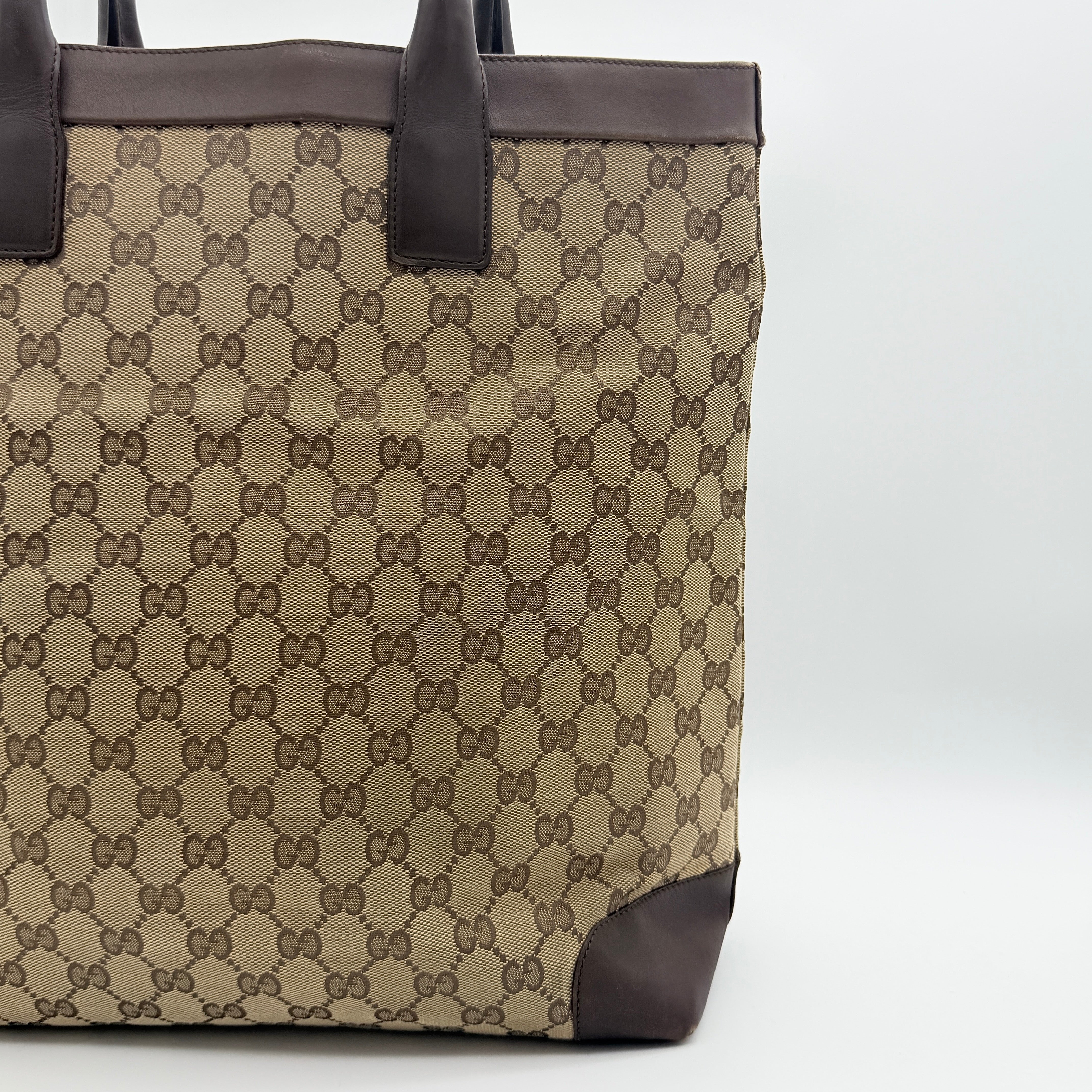Front view of a Gucci GG Monogram Tote Bag in beige and brown canvas with dark leather trim and structured handles.