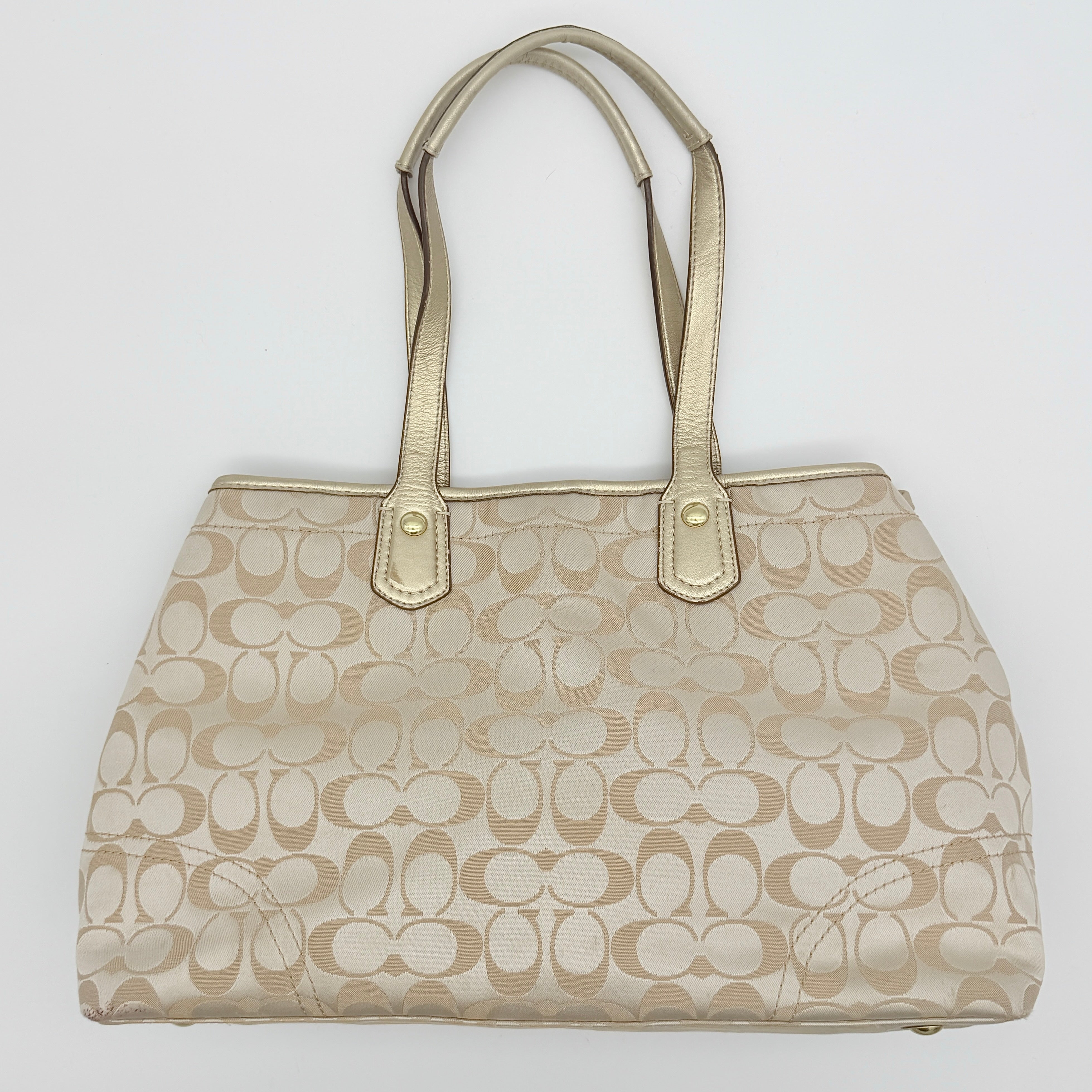 Coach beige carryall tote with floral appliqué and gold-tone handles, styled on a white background.