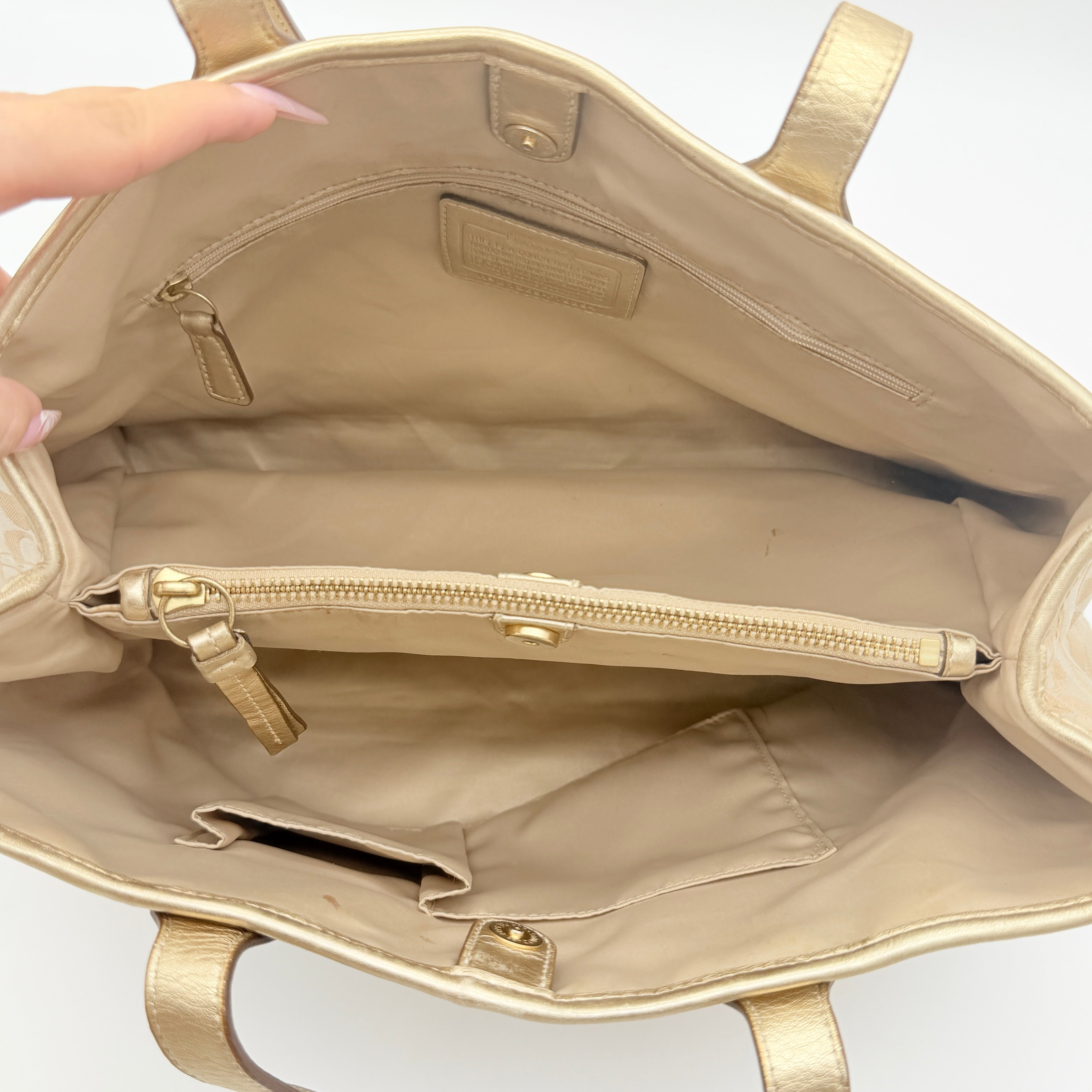 Coach beige carryall tote with floral appliqué and gold-tone handles, styled on a white background.