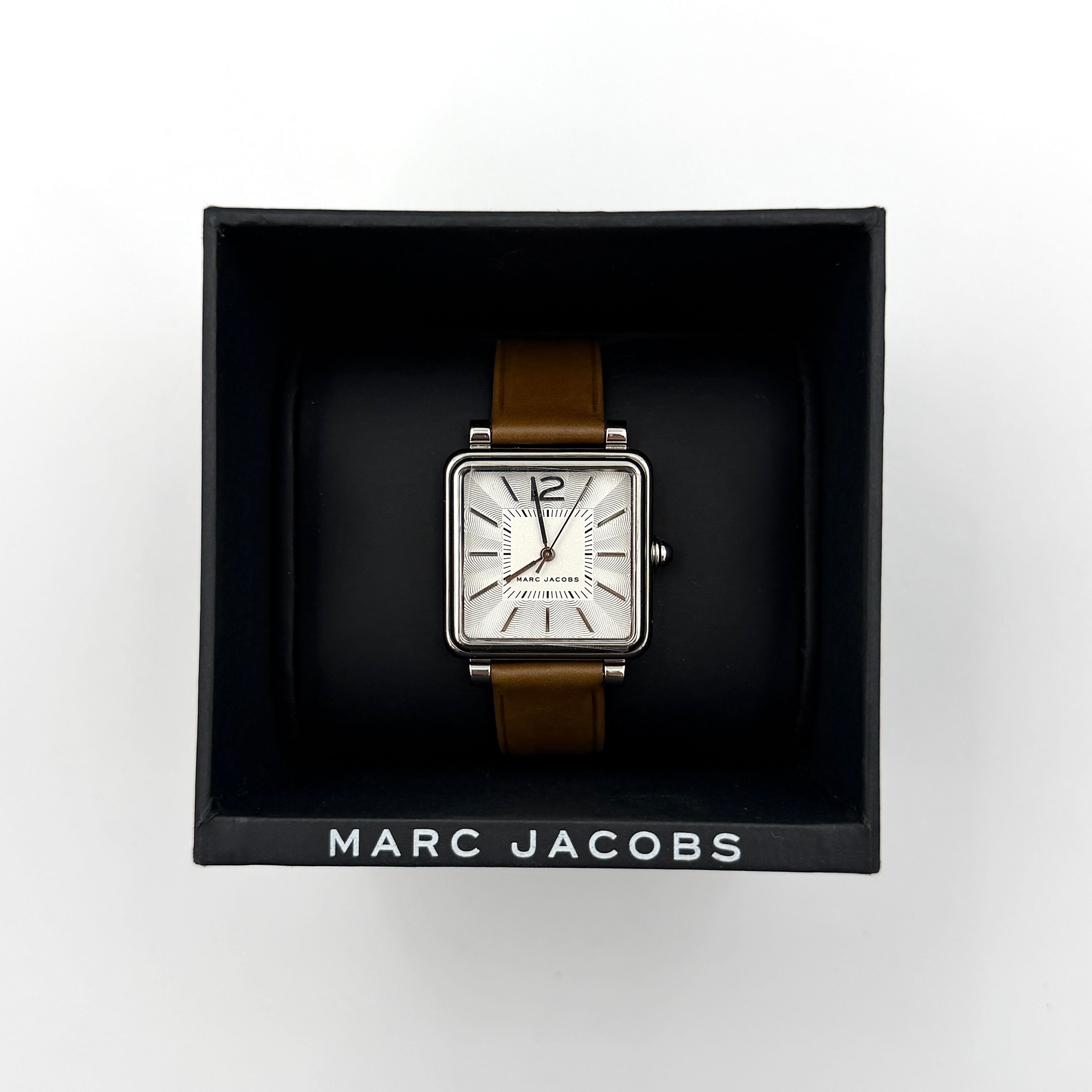 Marc Jacobs MJ1436 silver square watch with brown leather strap displayed on a branded watch cushion.