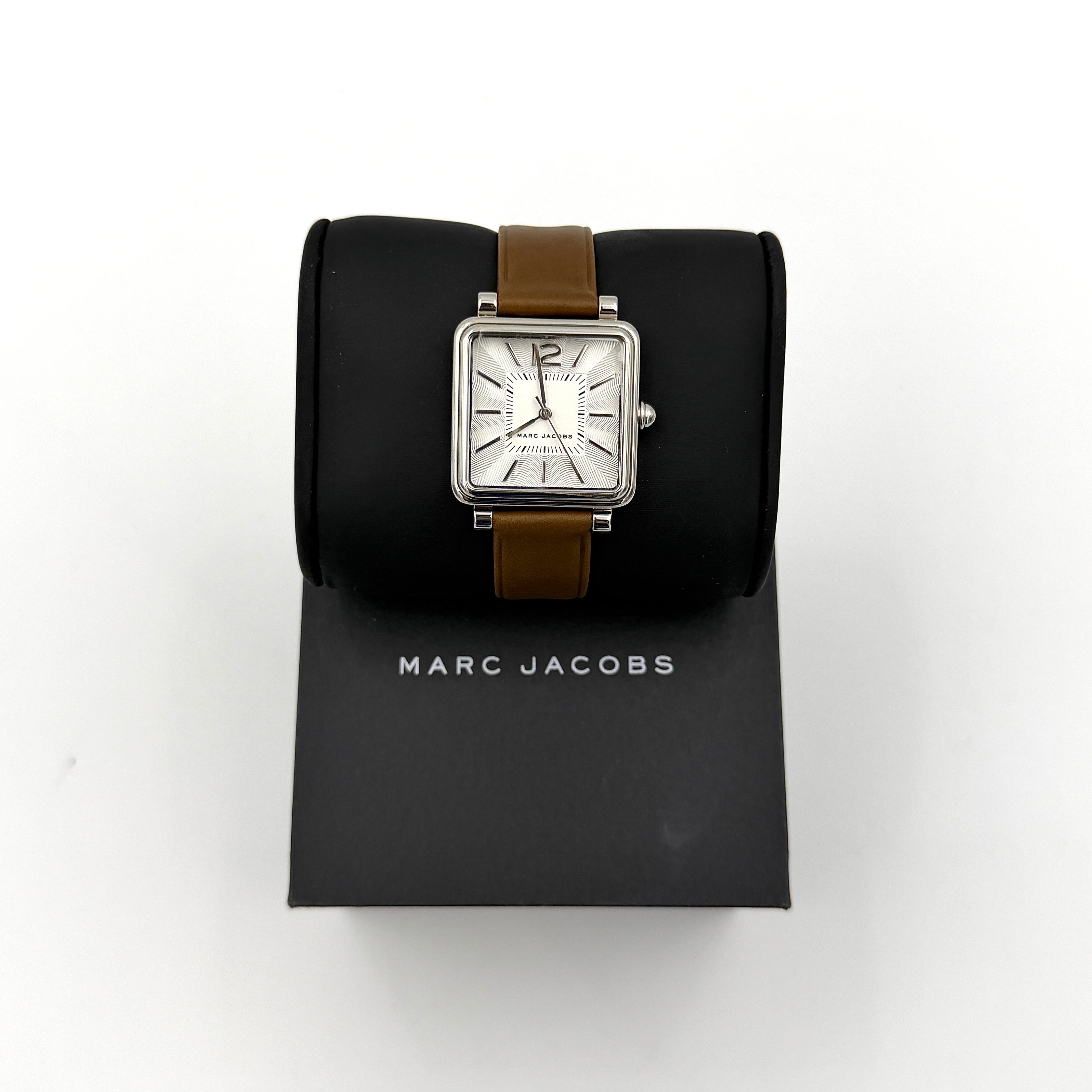 Marc Jacobs MJ1436 silver square watch with brown leather strap displayed on a branded watch cushion.
