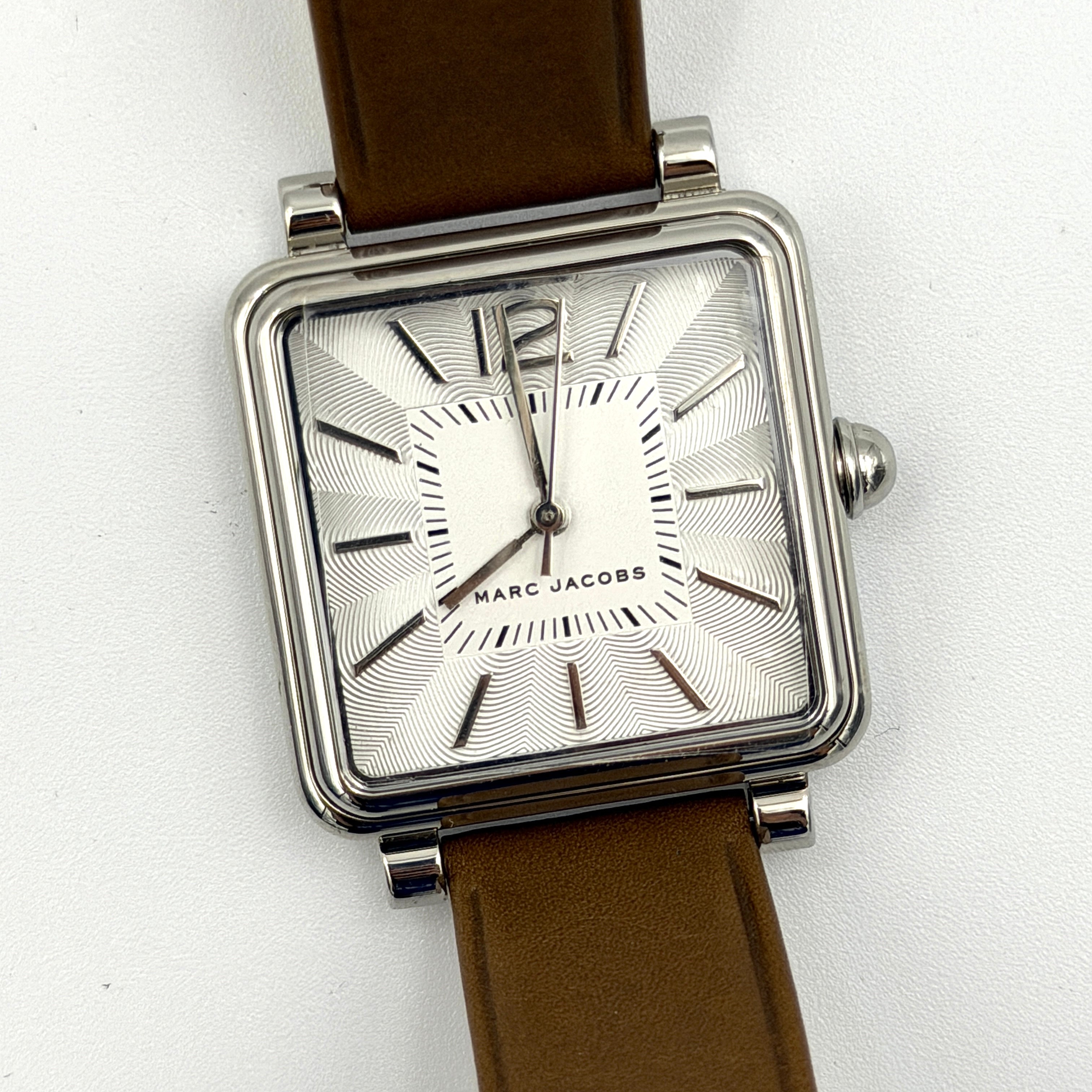 Marc Jacobs MJ1436 silver square watch with brown leather strap displayed on a branded watch cushion.