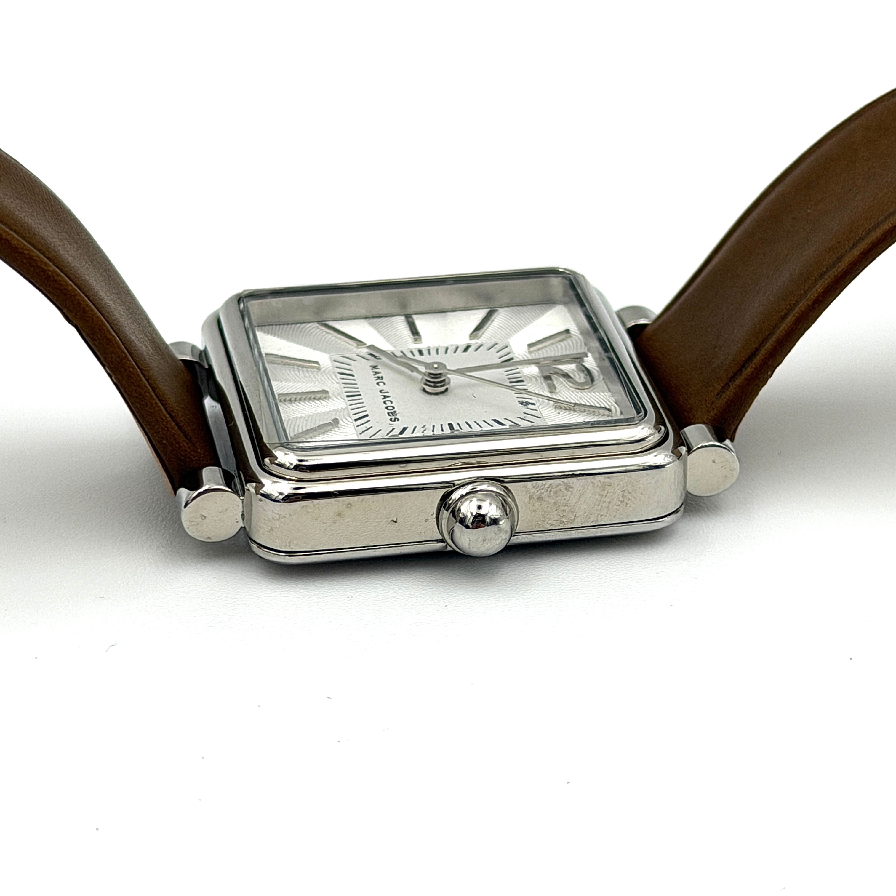 Marc Jacobs MJ1436 silver square watch with brown leather strap displayed on a branded watch cushion.