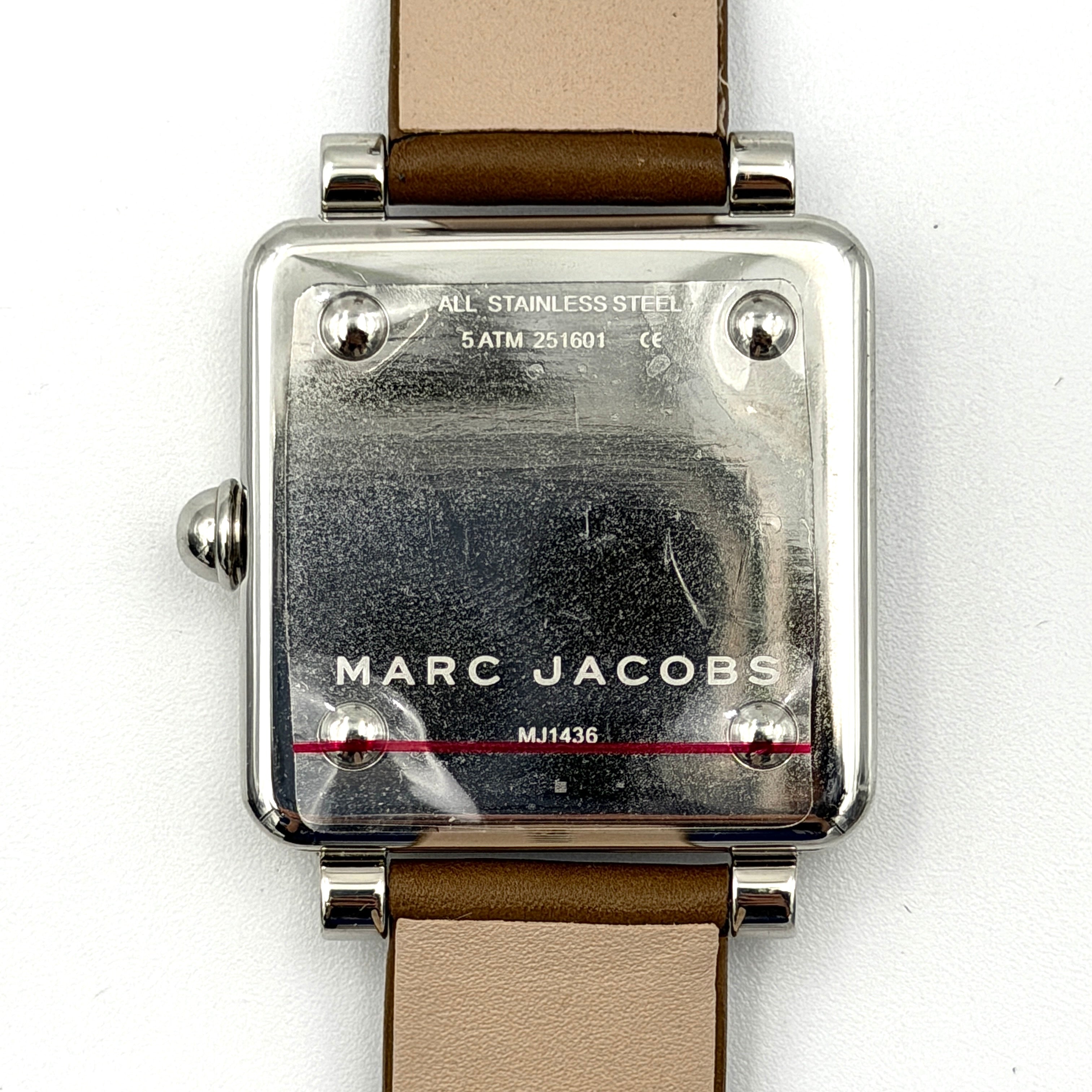 Marc Jacobs MJ1436 silver square watch with brown leather strap displayed on a branded watch cushion.