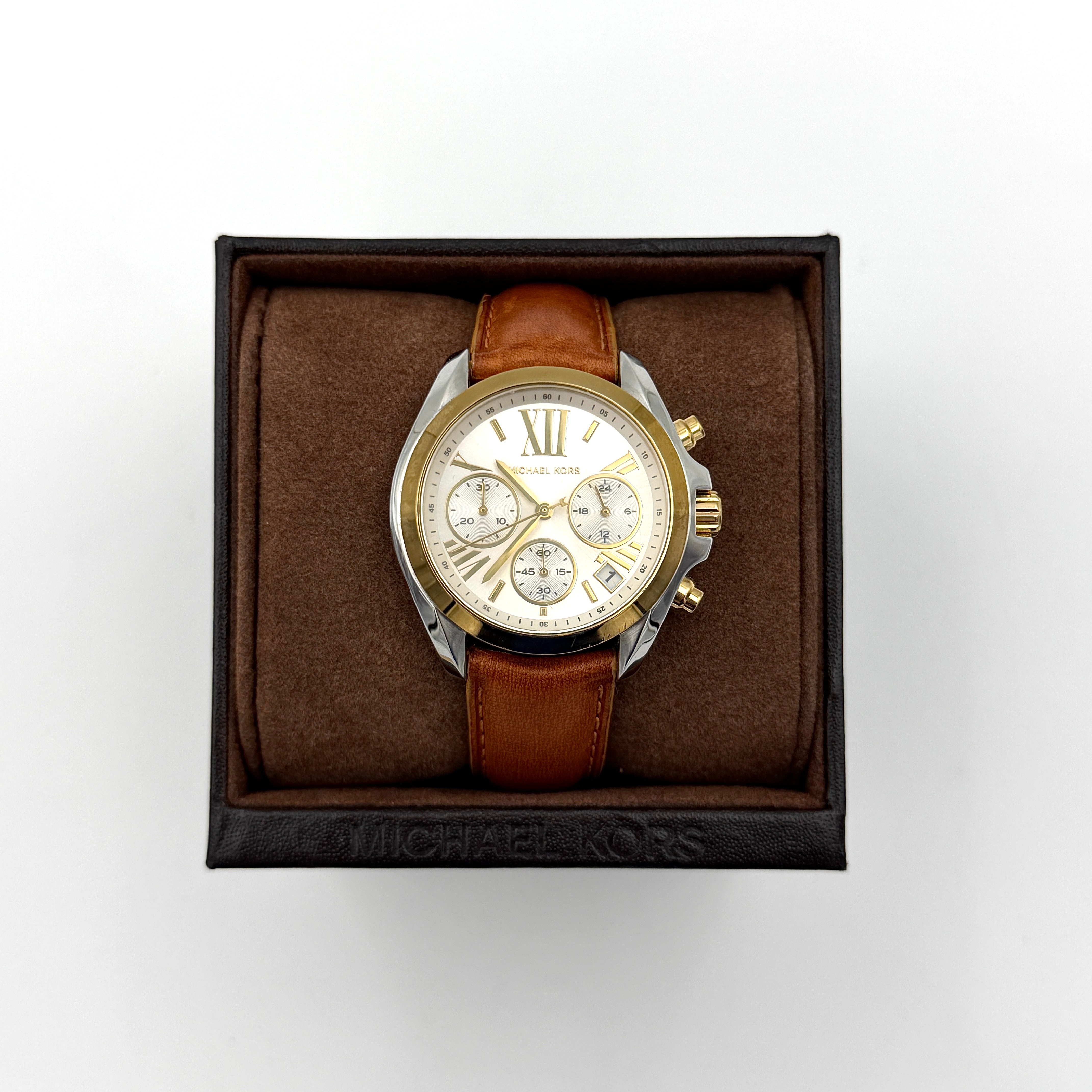 Michael Kors MK-2301 gold and silver tone chronograph watch with brown leather strap, showcased on a brown cushion atop the branded box.