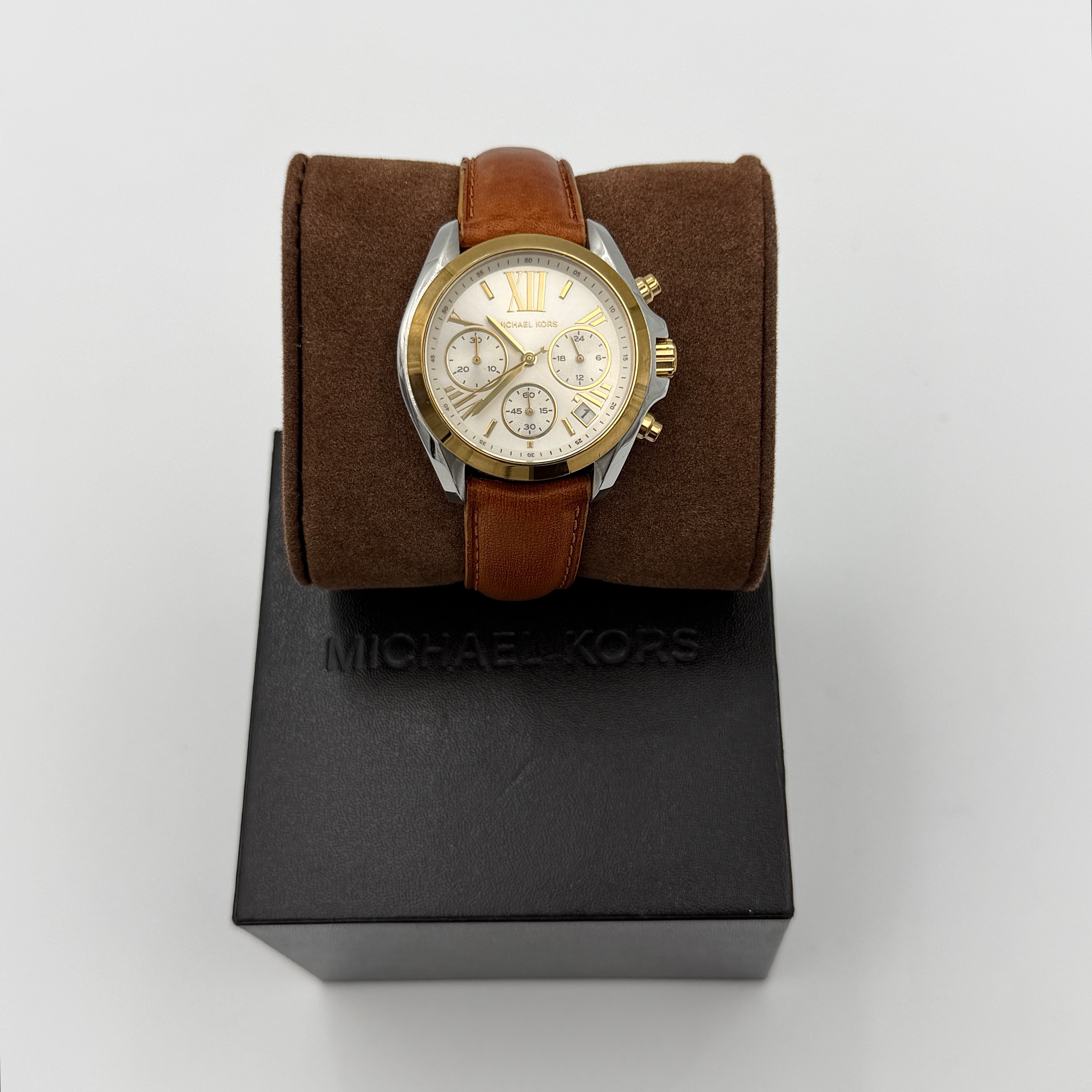 Michael Kors MK-2301 gold and silver tone chronograph watch with brown leather strap, showcased on a brown cushion atop the branded box.
