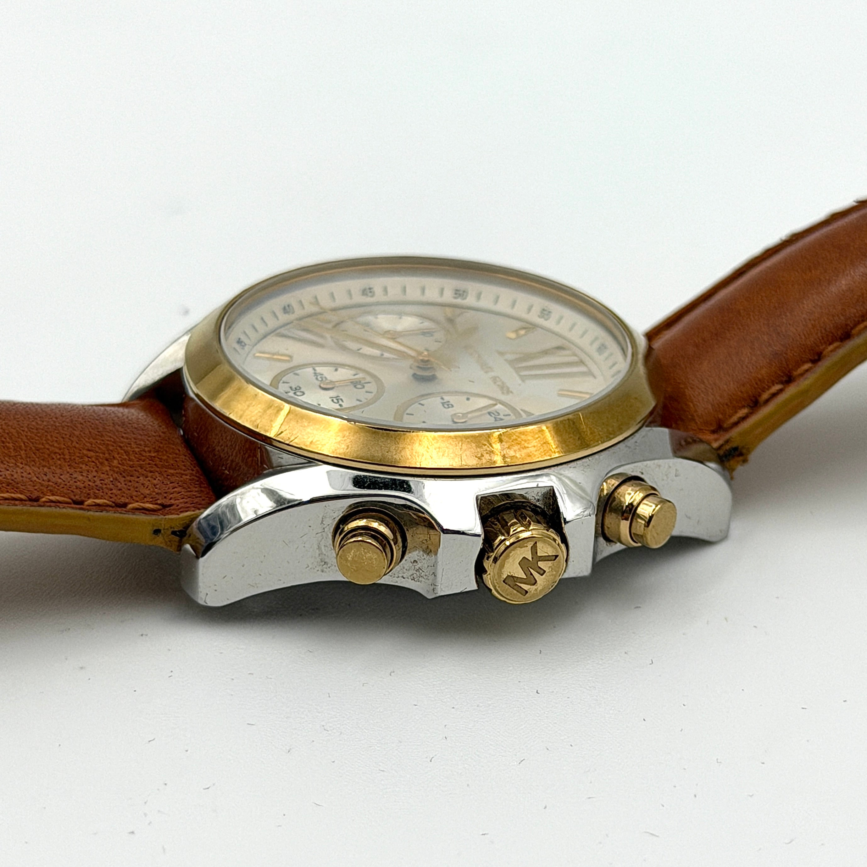 Michael Kors MK-2301 gold and silver tone chronograph watch with brown leather strap, showcased on a brown cushion atop the branded box.