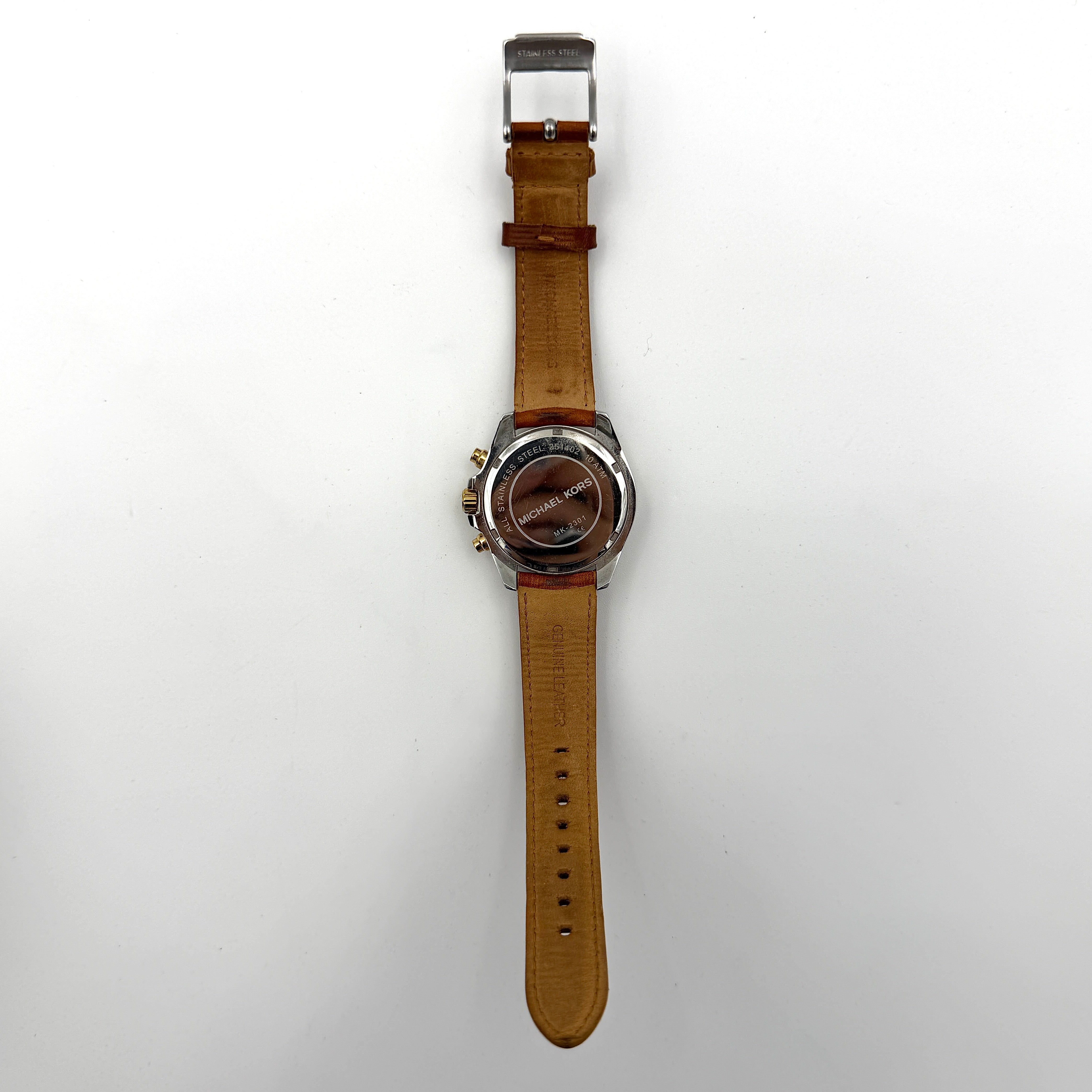 Michael Kors MK-2301 gold and silver tone chronograph watch with brown leather strap, showcased on a brown cushion atop the branded box.