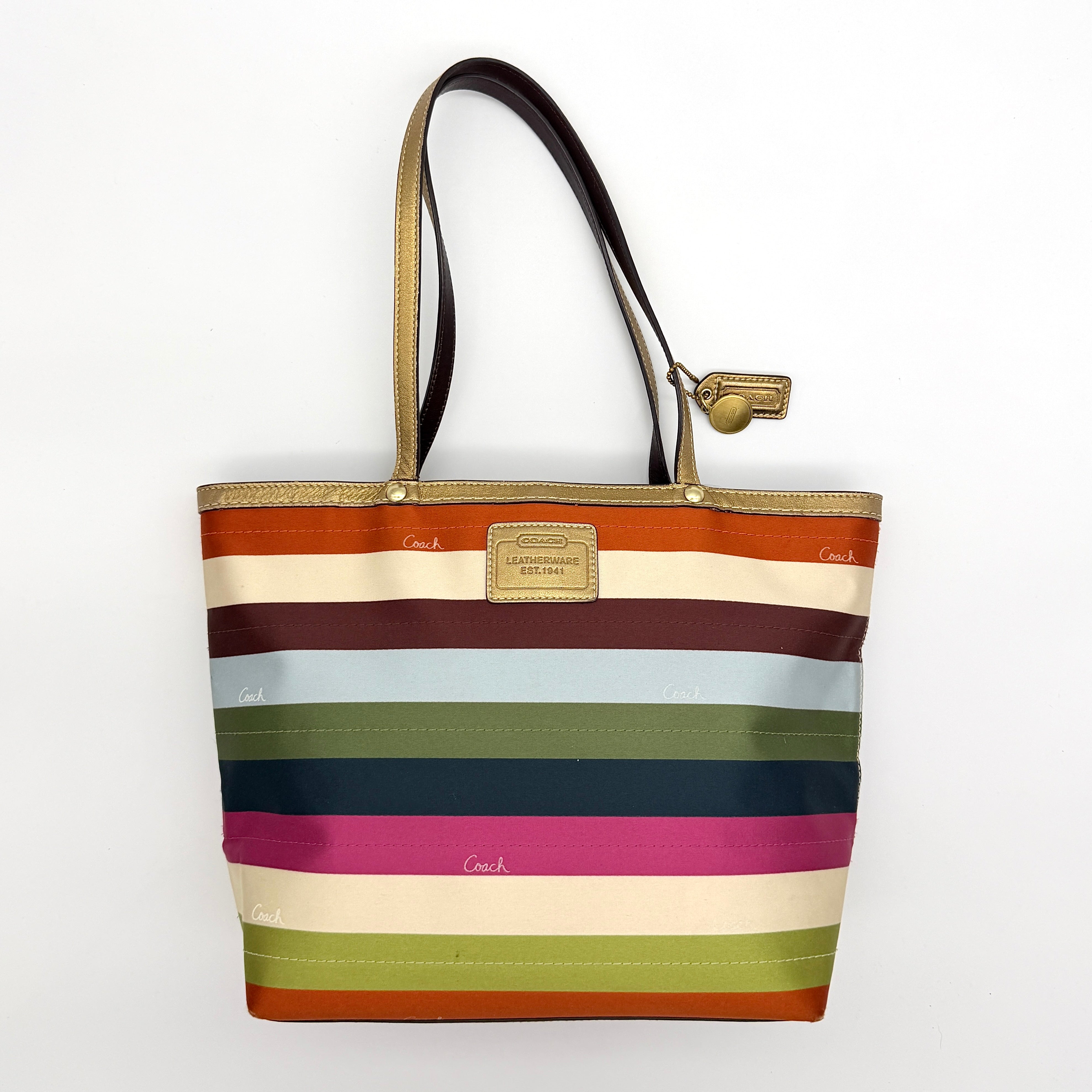 Coach Legacy Stripe Tote Bag in multicolour stripes with gold leather trim and double handles, displayed against a white background.