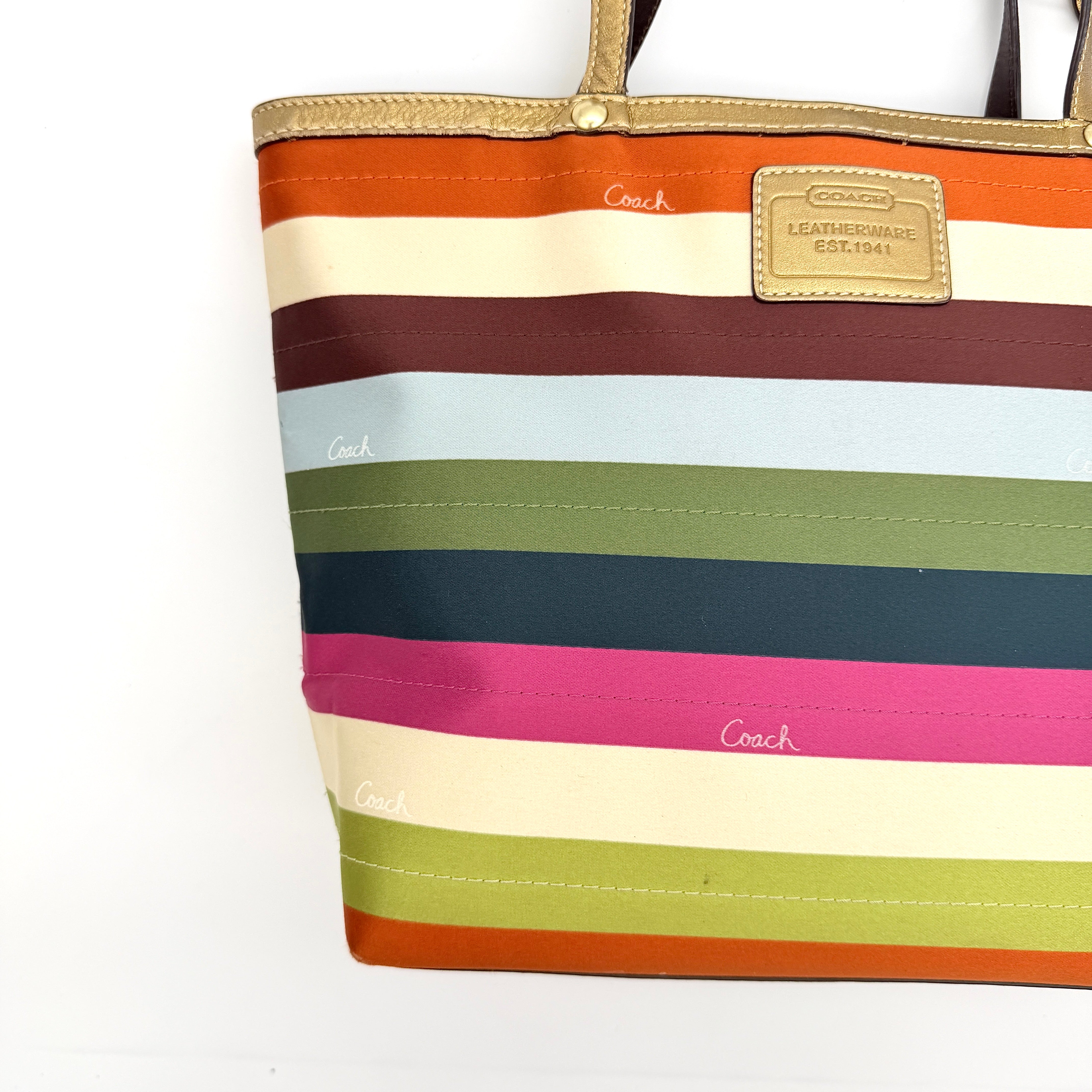 Coach Legacy Stripe Tote Bag in multicolour stripes with gold leather trim and double handles, displayed against a white background.