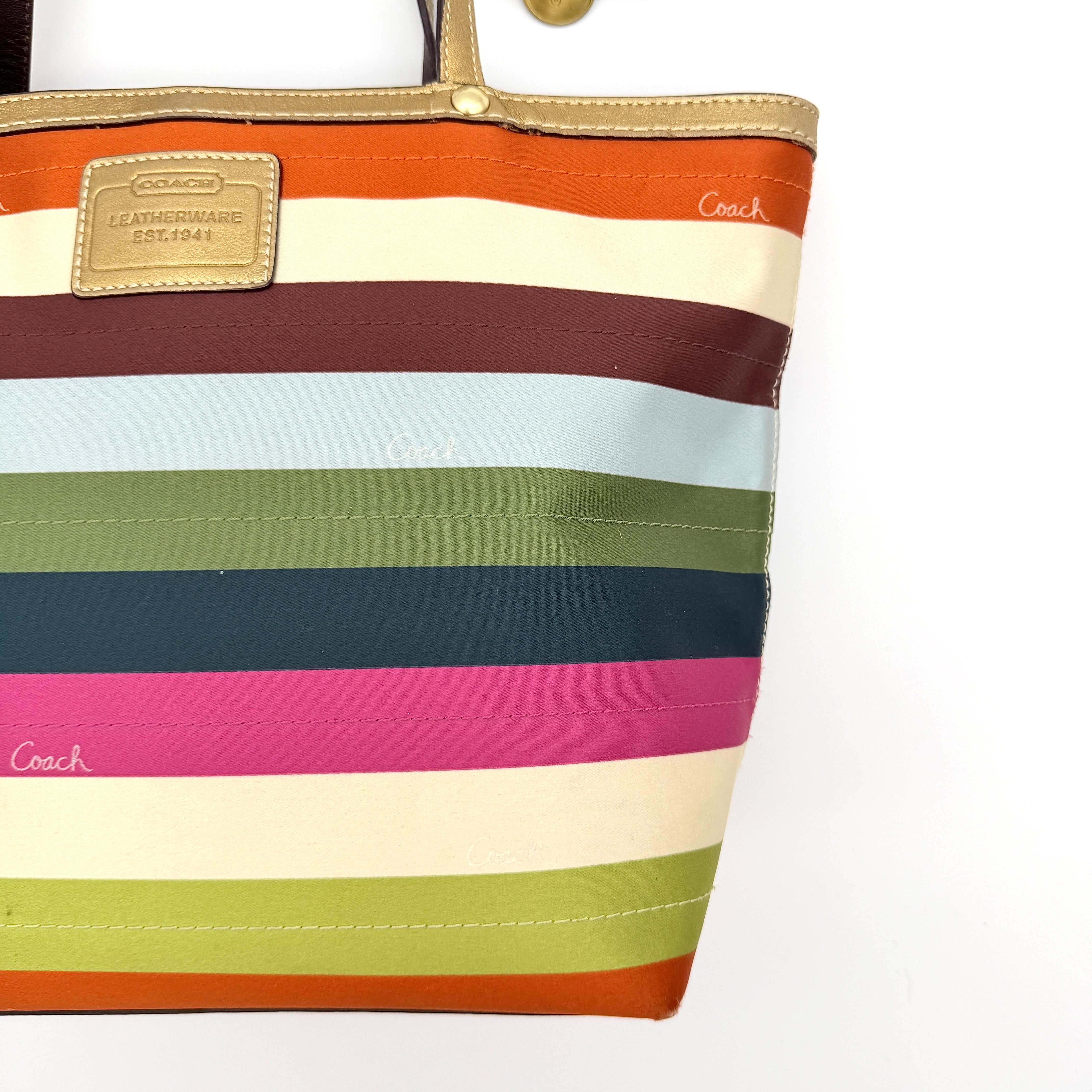 Coach Legacy Stripe Tote Bag in multicolour stripes with gold leather trim and double handles, displayed against a white background.