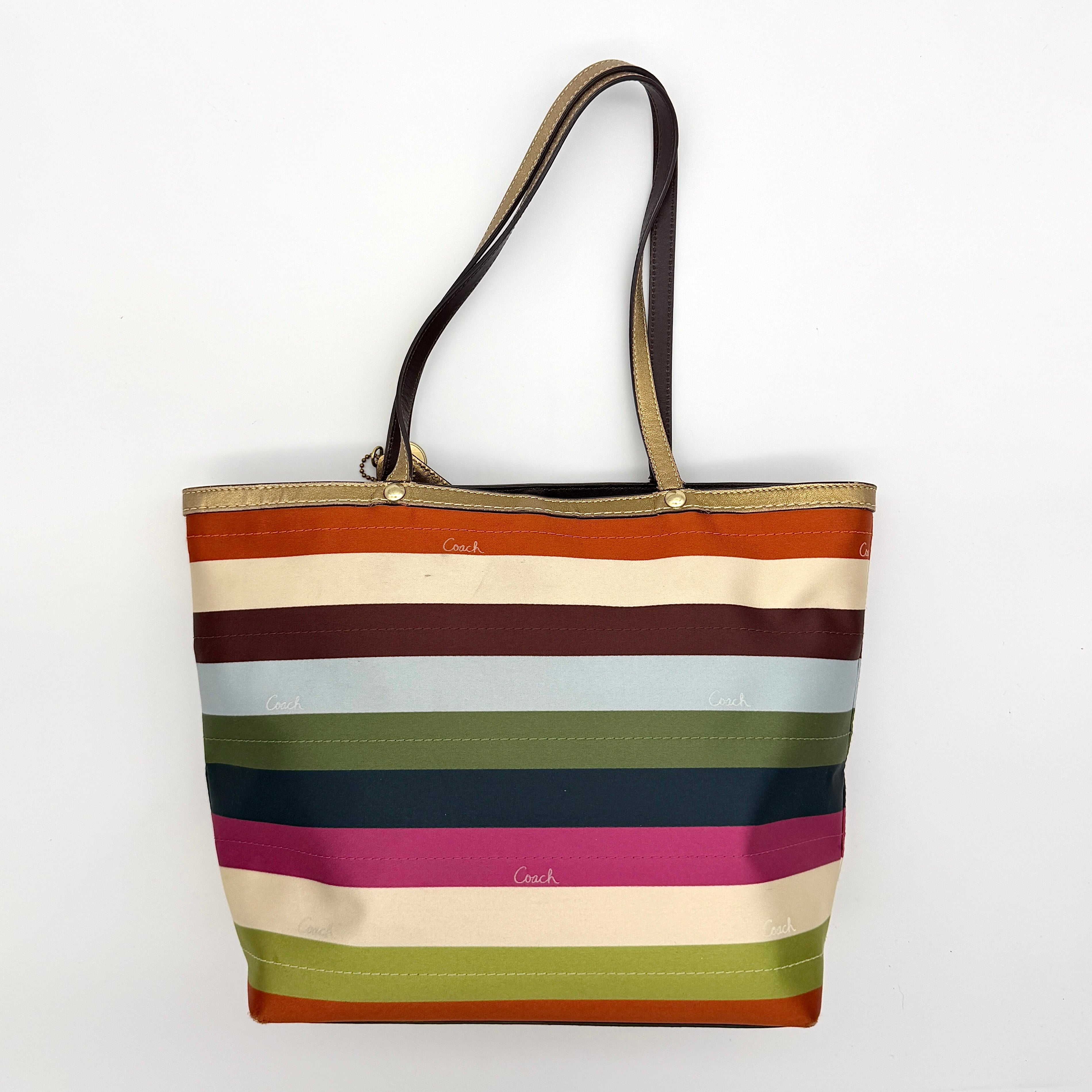 Coach Legacy Stripe Tote Bag in multicolour stripes with gold leather trim and double handles, displayed against a white background.