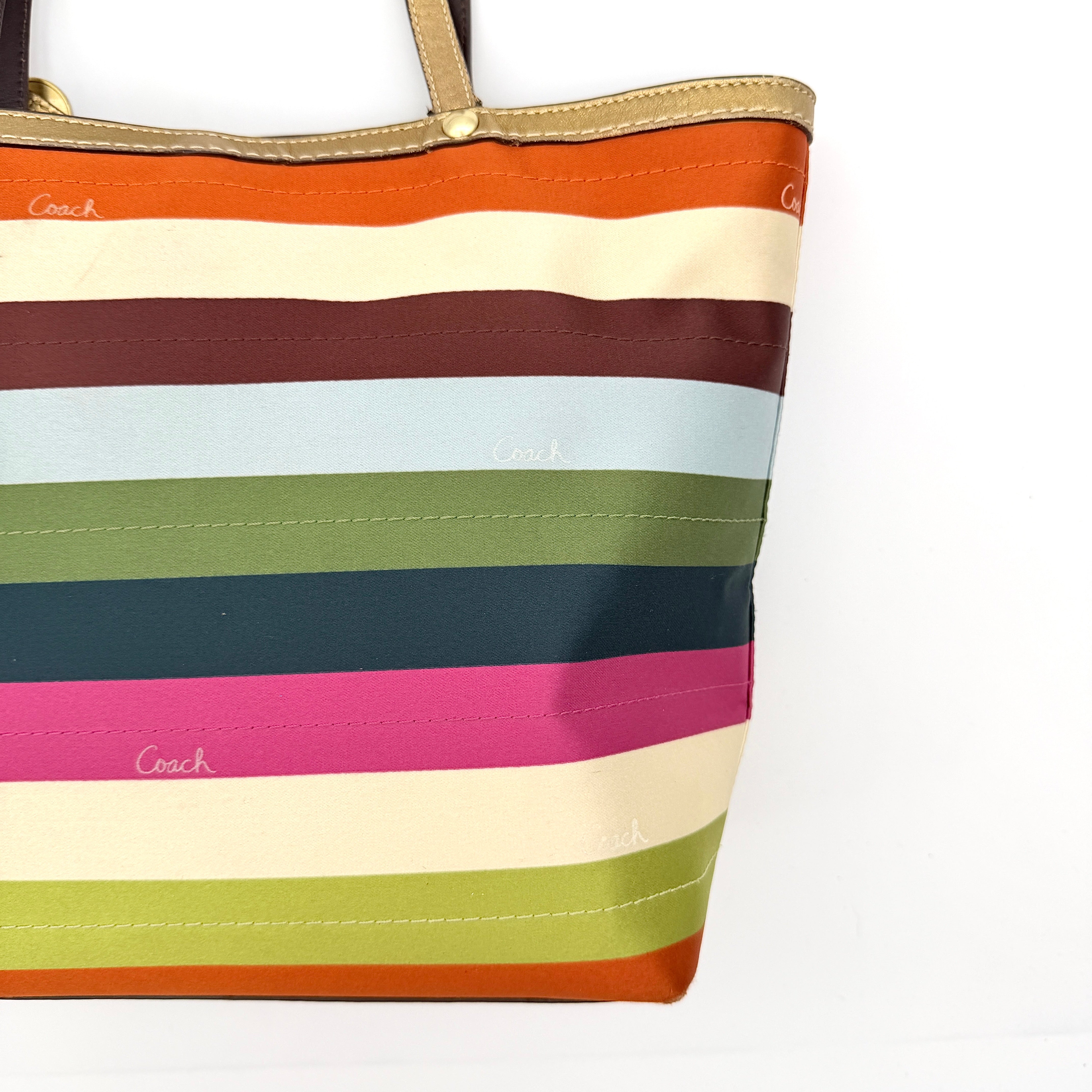 Coach Legacy Stripe Tote Bag in multicolour stripes with gold leather trim and double handles, displayed against a white background.