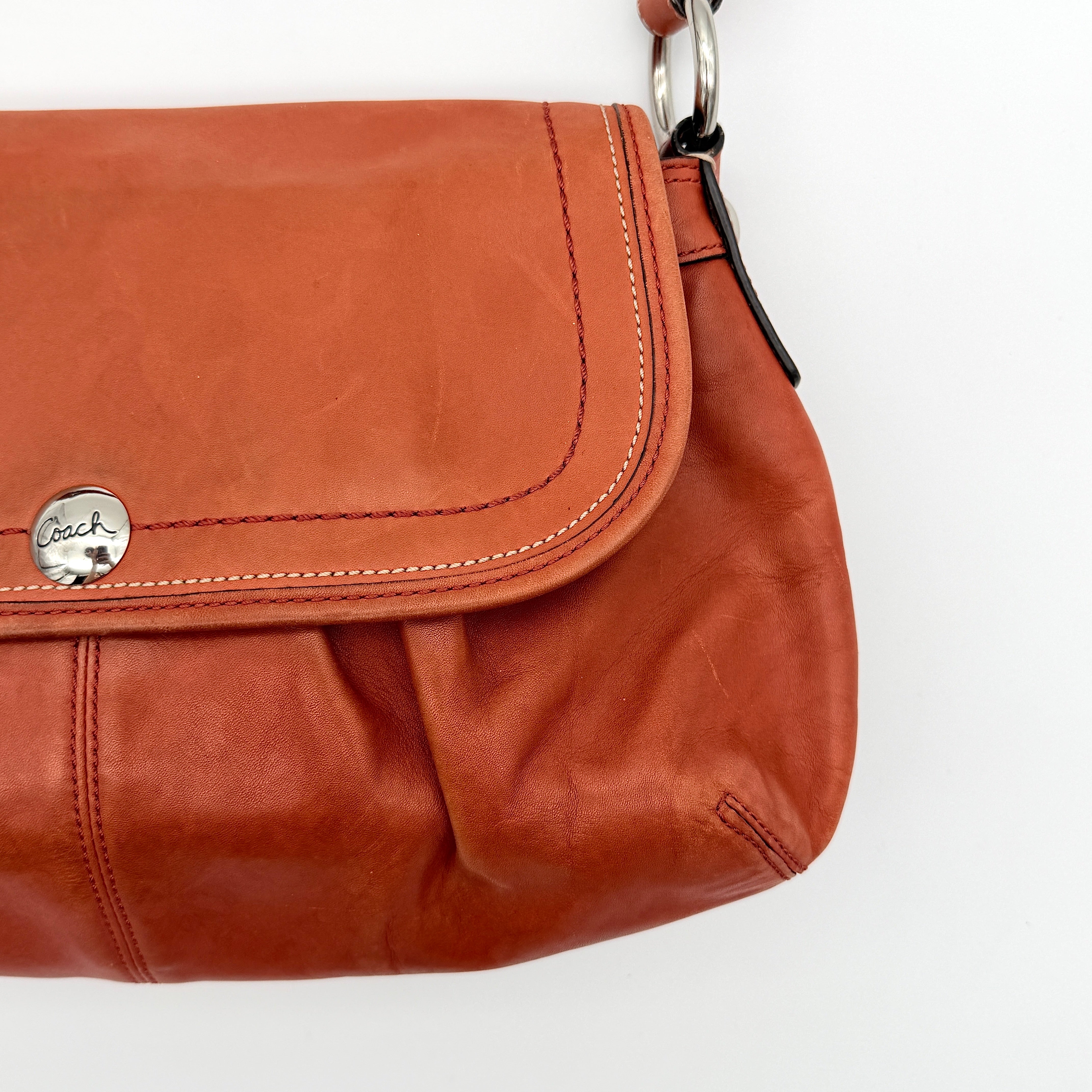 Coach Soho bag in burnt orange leather with pleated detailing and wide shoulder strap, shown on a white background.