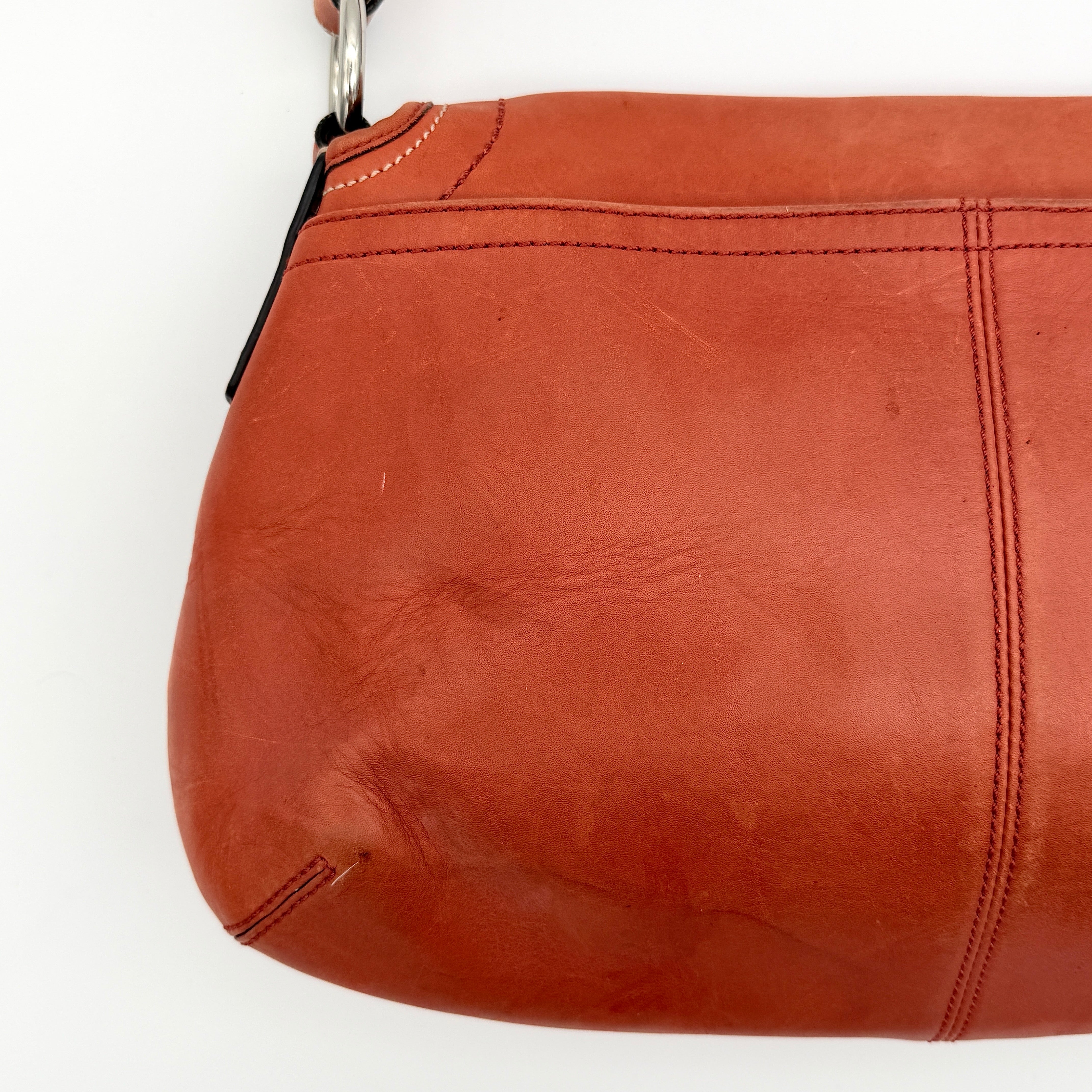 Coach Soho bag in burnt orange leather with pleated detailing and wide shoulder strap, shown on a white background.