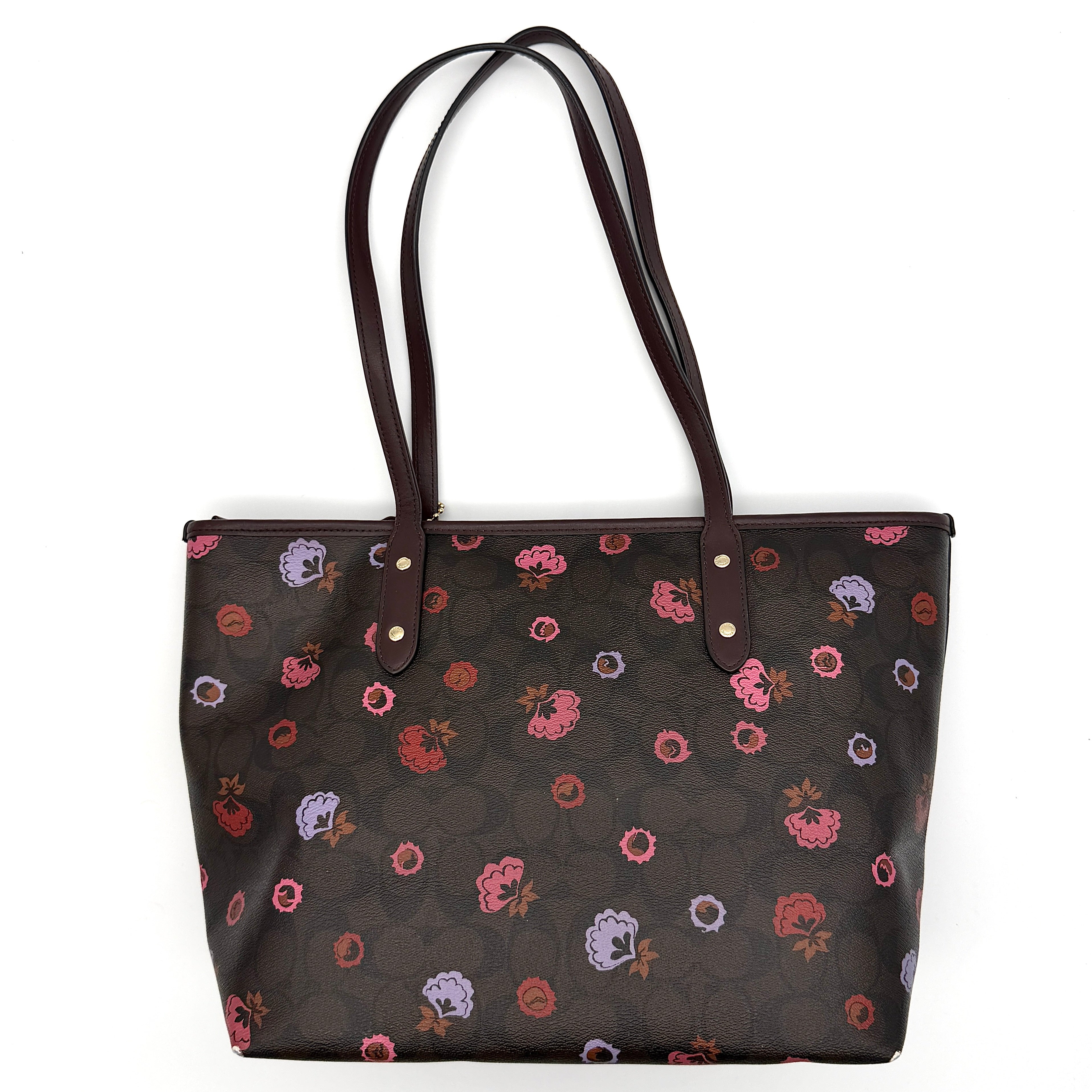 Coach brown coated canvas city tote with pink and lavender floral print, burgundy handles, and gold-tone logo at the front.