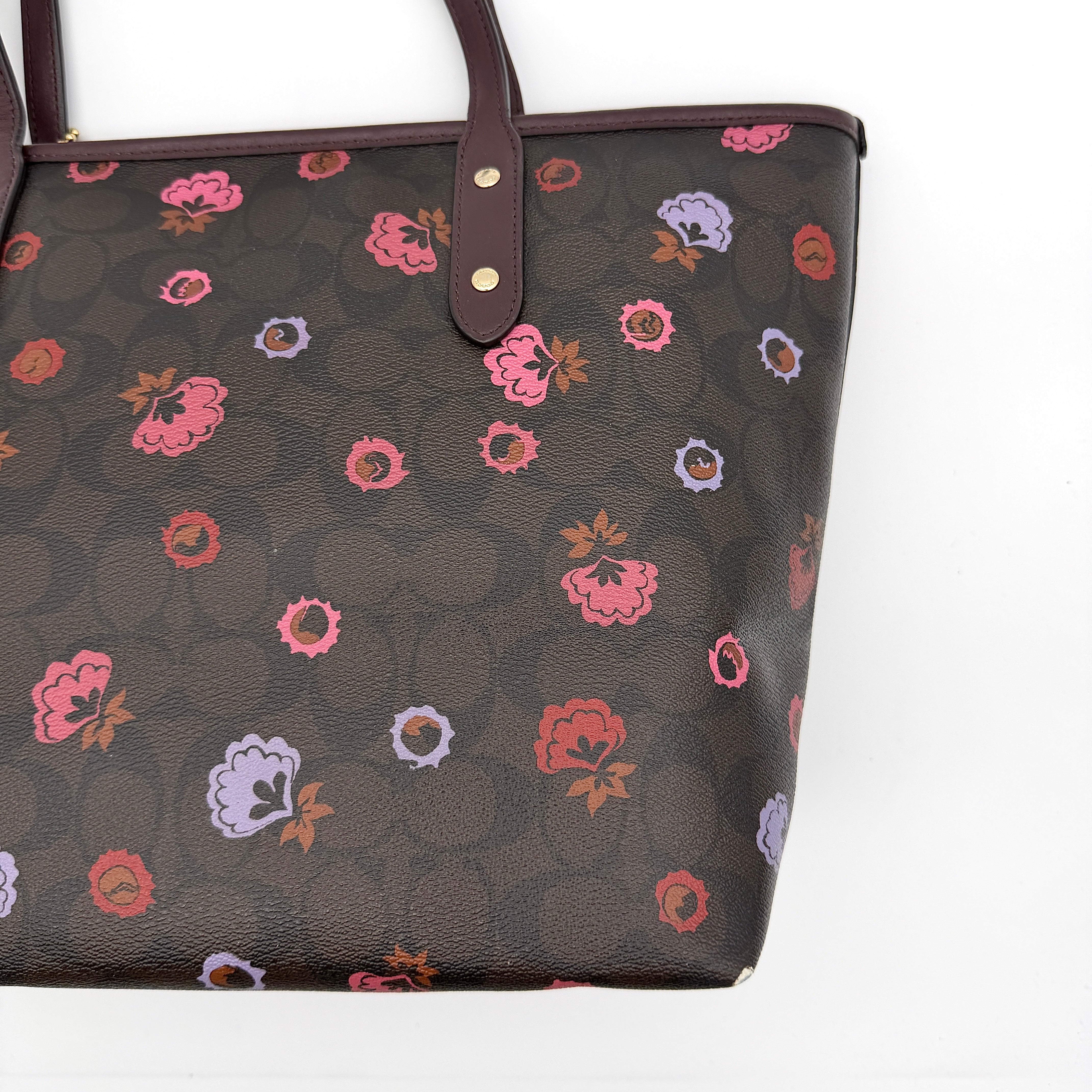 Coach brown coated canvas city tote with pink and lavender floral print, burgundy handles, and gold-tone logo at the front.