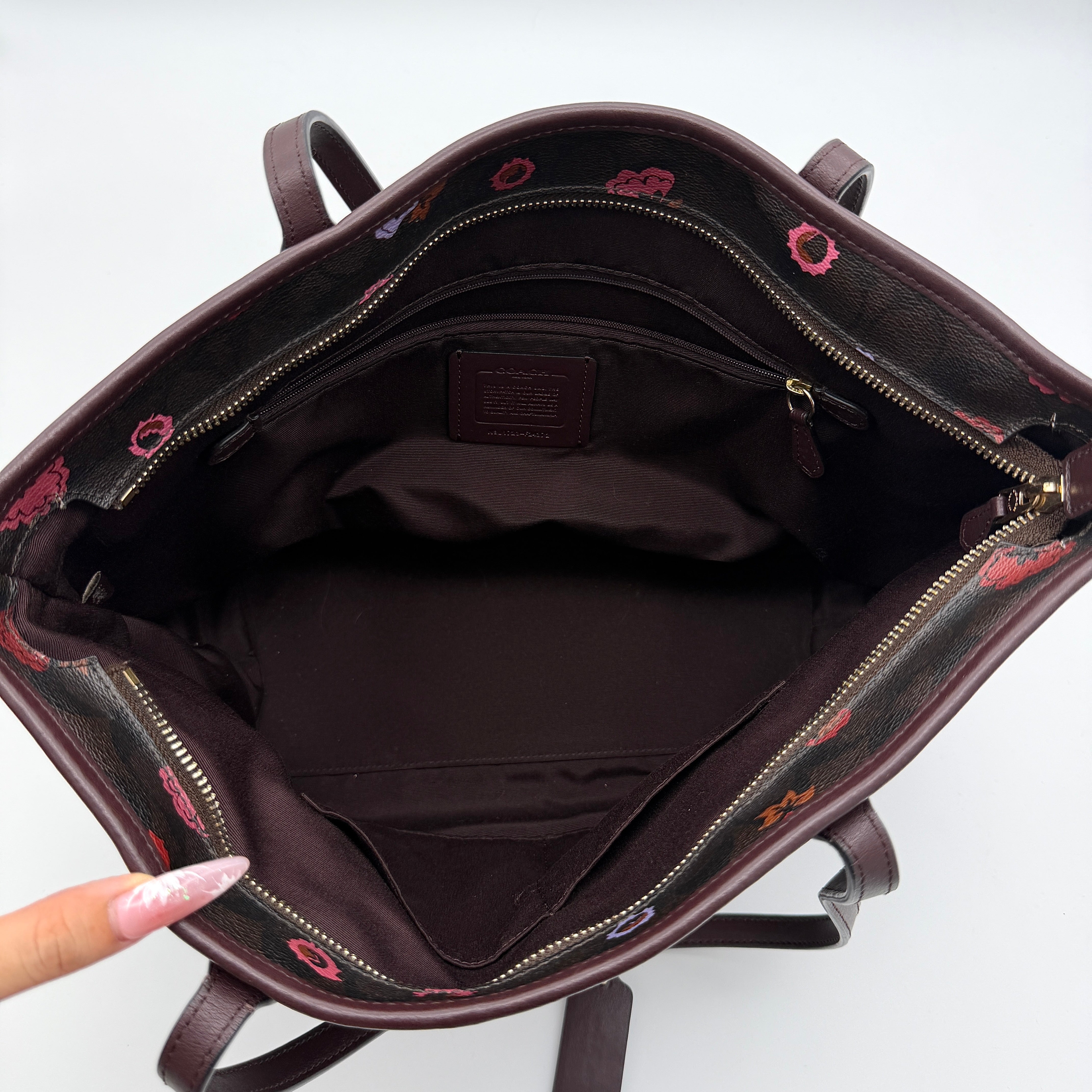 Coach brown coated canvas city tote with pink and lavender floral print, burgundy handles, and gold-tone logo at the front.