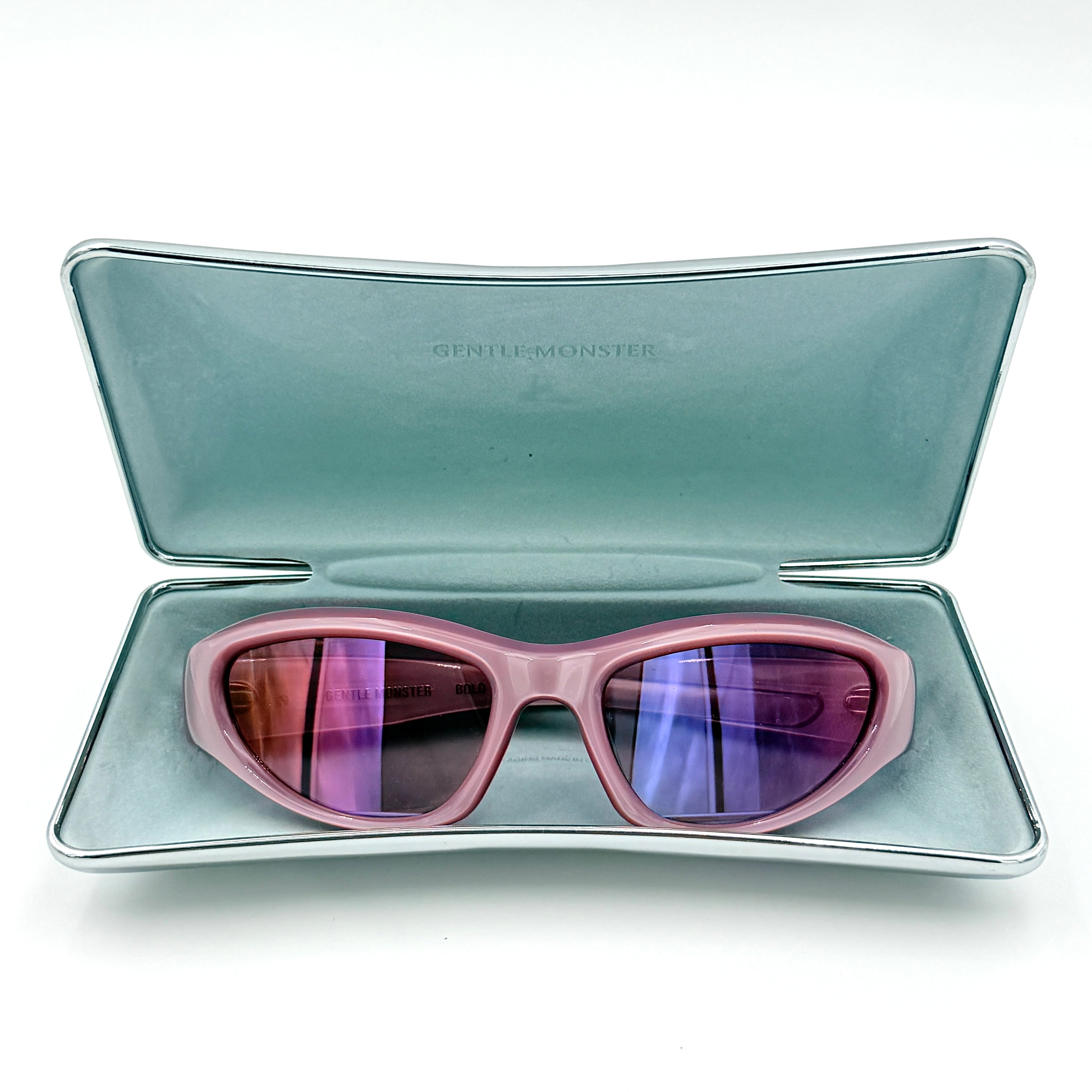 Gentle Monster R.E.A.T sunglasses in translucent pink acetate with mirrored pink lenses and silver star hardware, displayed alongside a chrome hard case.