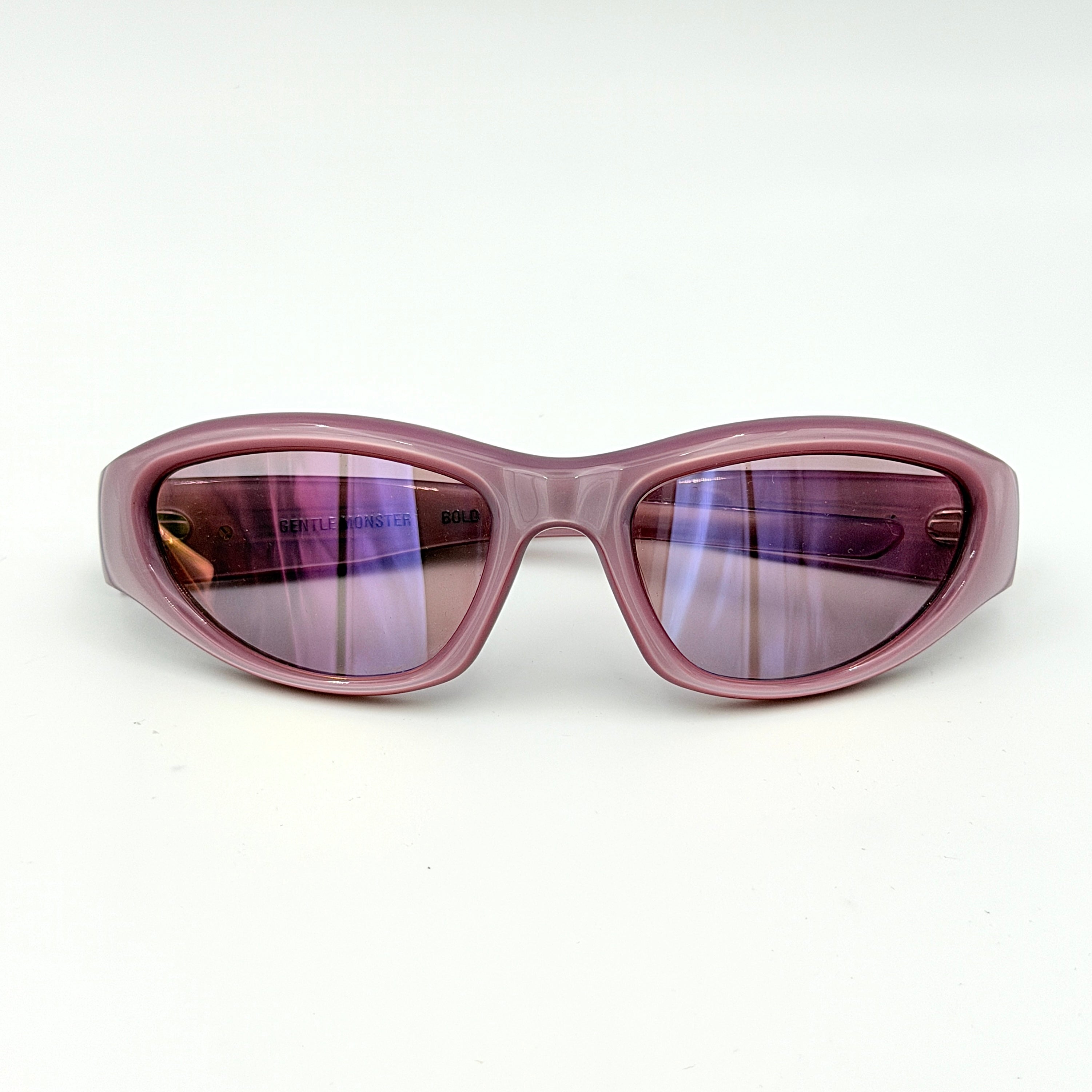 Gentle Monster R.E.A.T sunglasses in translucent pink acetate with mirrored pink lenses and silver star hardware, displayed alongside a chrome hard case.
