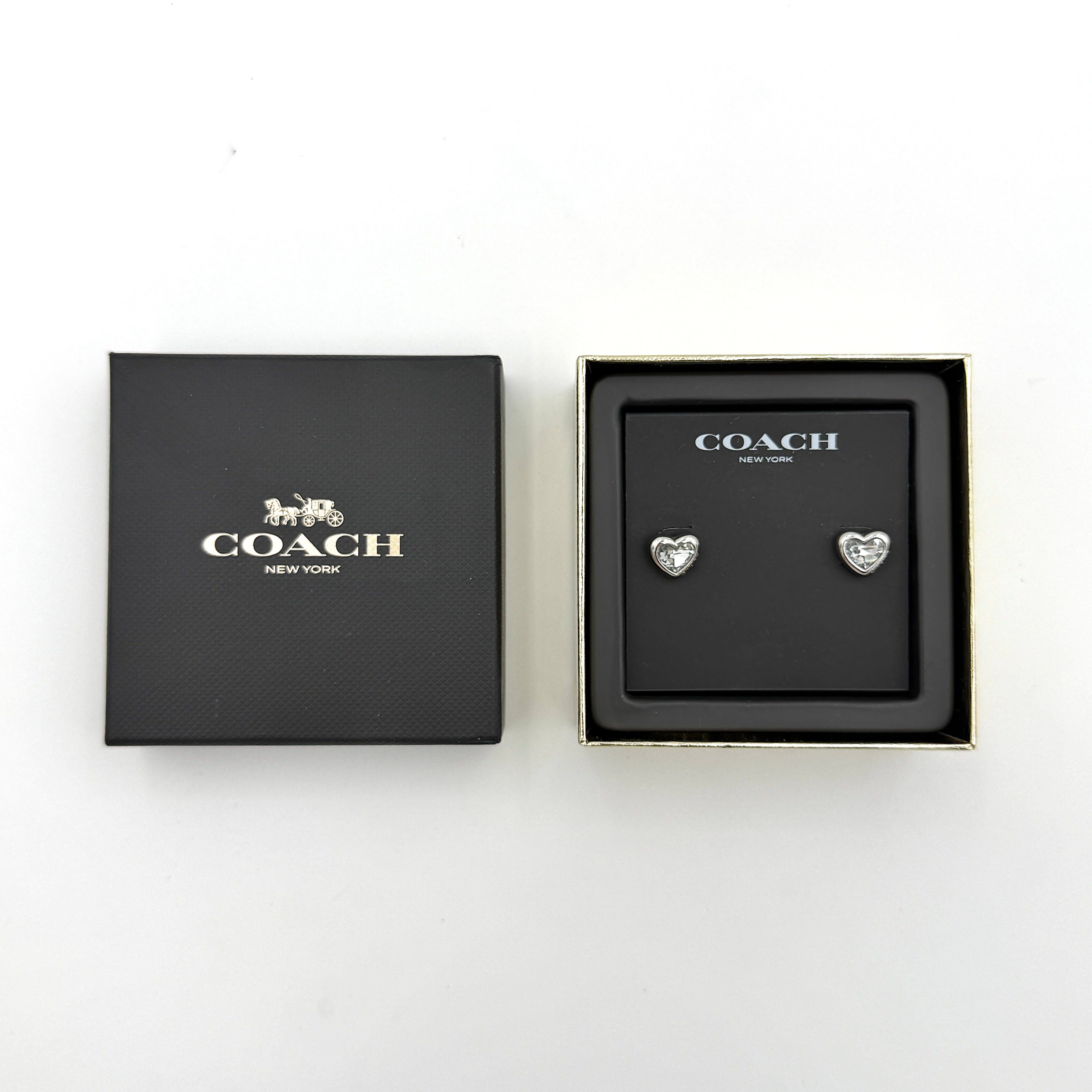 A pair of Coach heart-shaped crystal stud earrings in silver-tone metal with engraved logo and faceted stones.