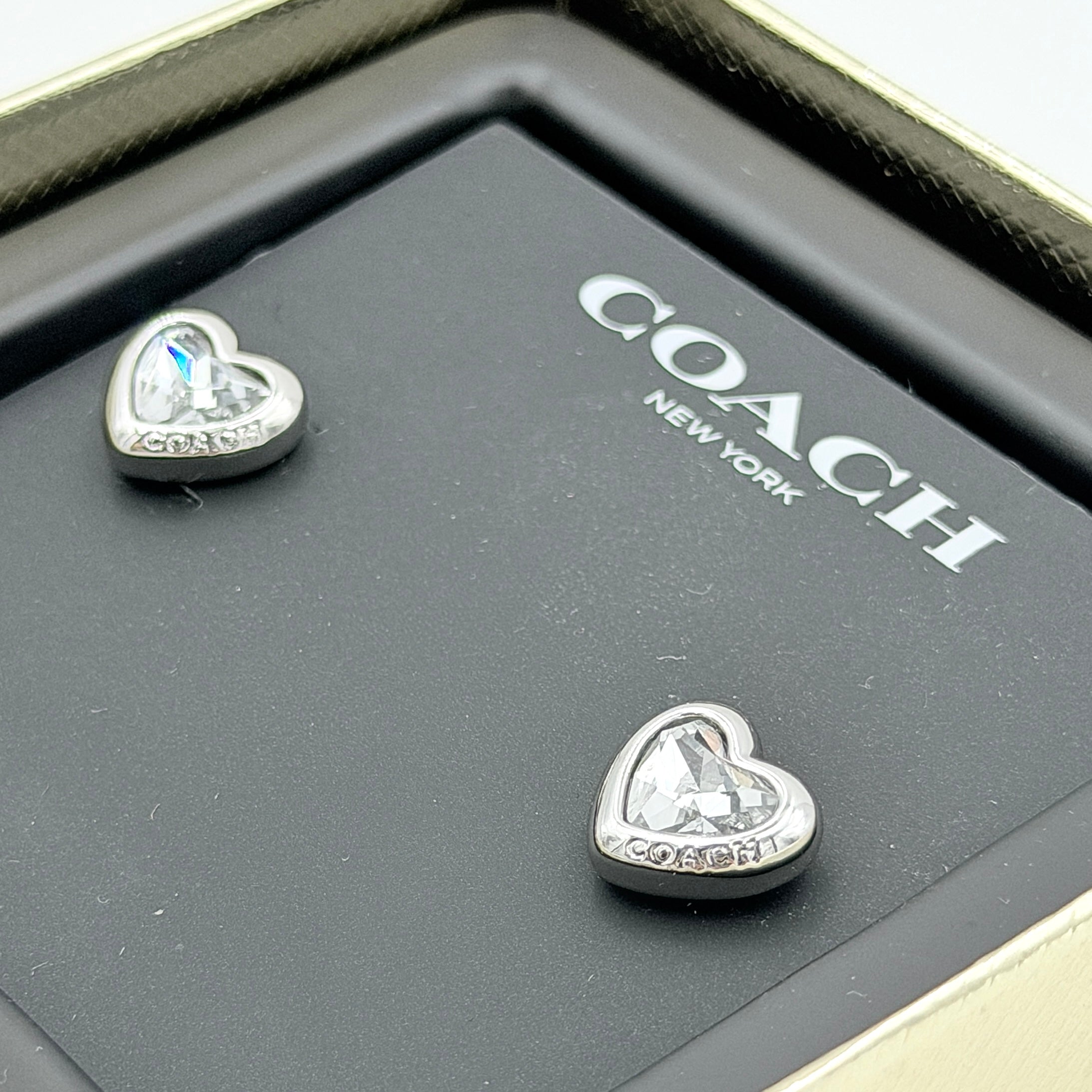 A pair of Coach heart-shaped crystal stud earrings in silver-tone metal with engraved logo and faceted stones.