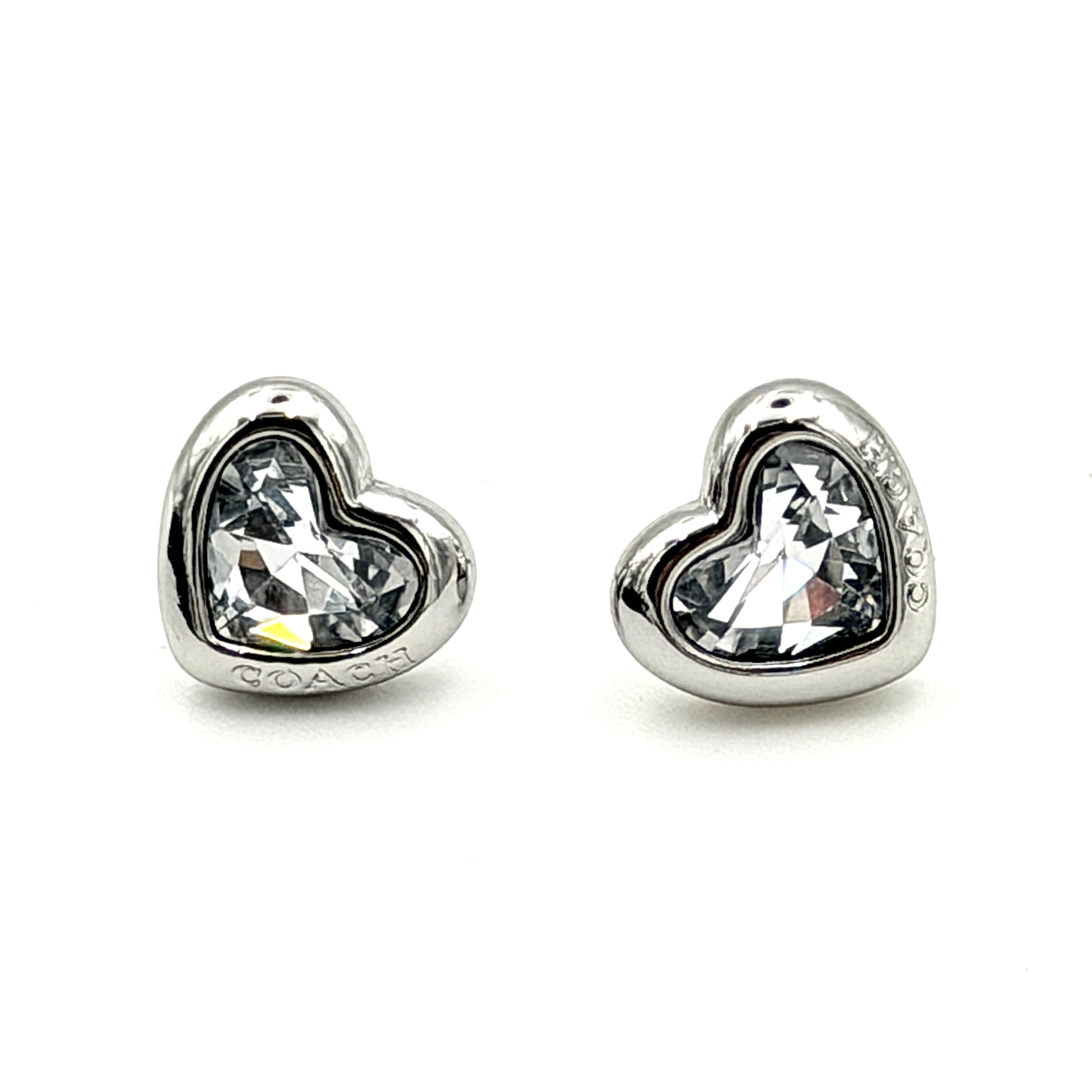 A pair of Coach heart-shaped crystal stud earrings in silver-tone metal with engraved logo and faceted stones.