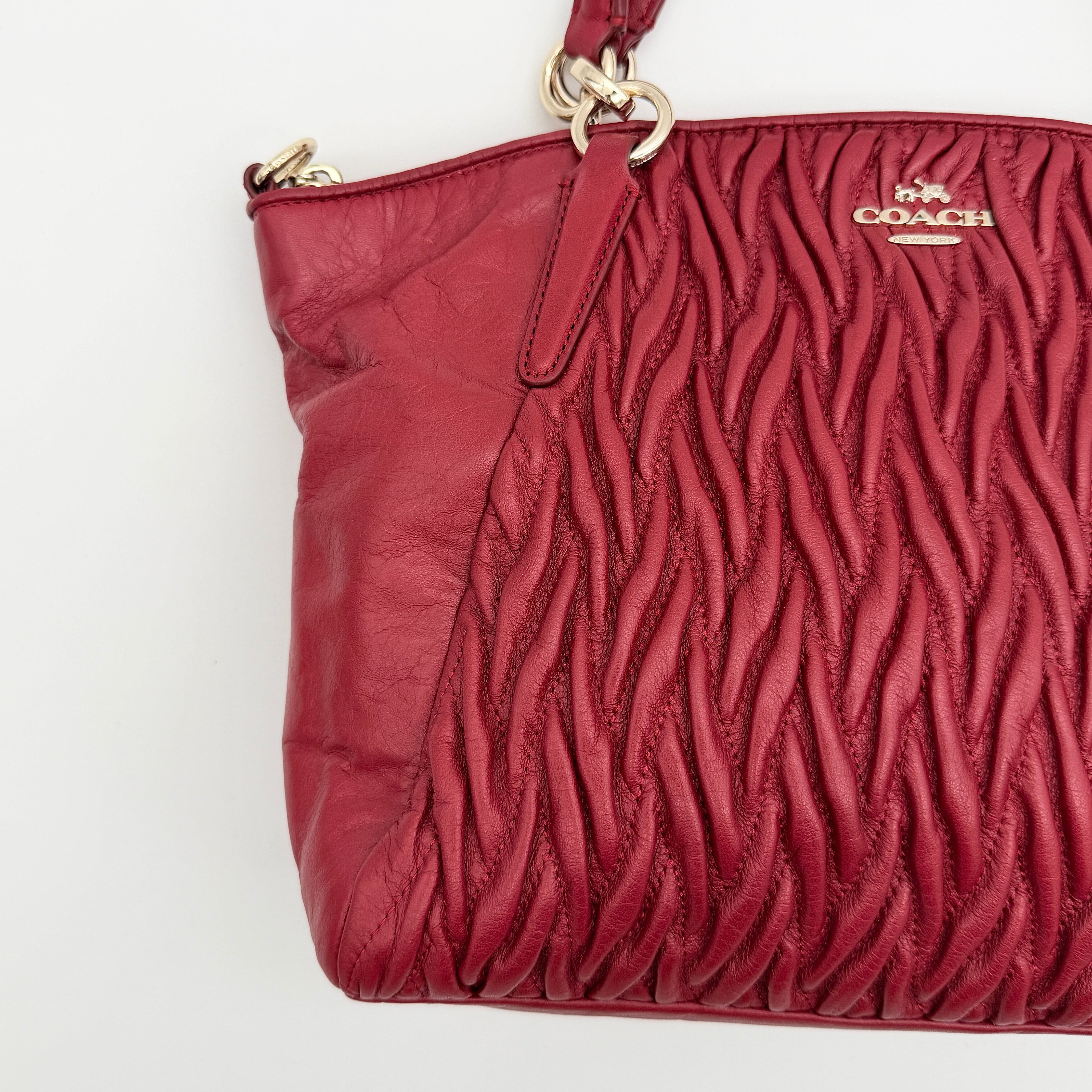 Coach Kelsey 2Way satchel in quilted red leather with gold-tone hardware and detachable strap, displayed against a white background.