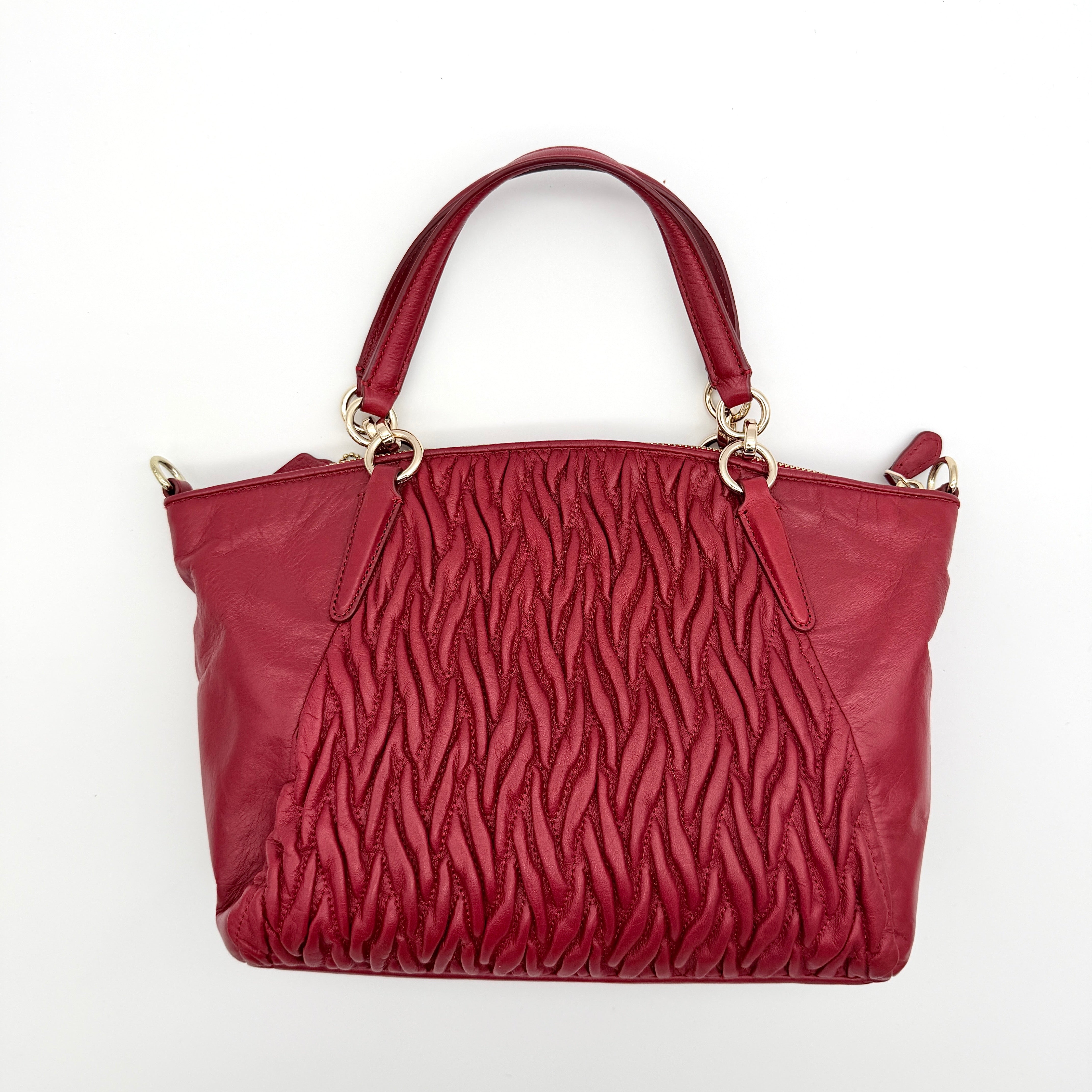 Coach Kelsey 2Way satchel in quilted red leather with gold-tone hardware and detachable strap, displayed against a white background.