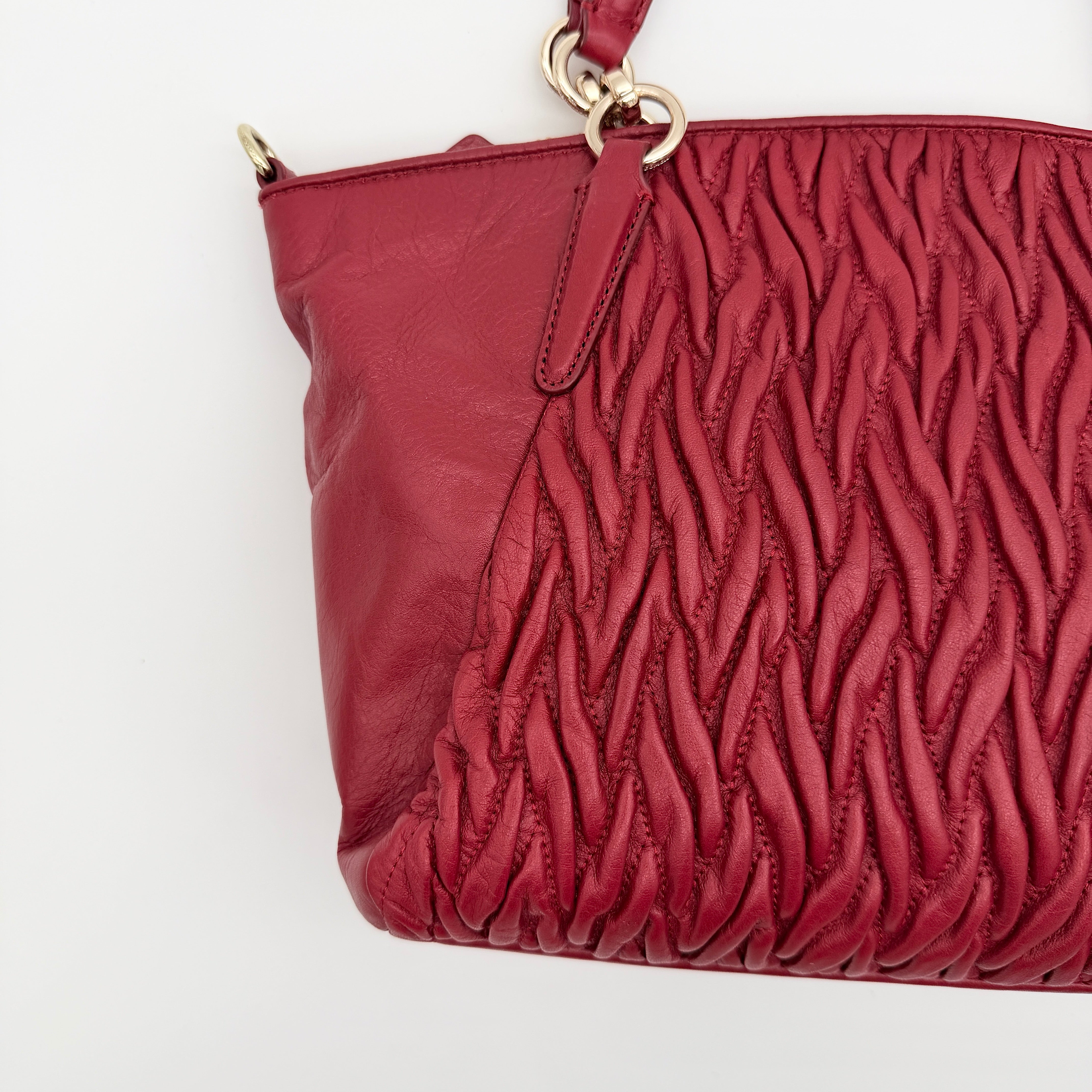 Coach Kelsey 2Way satchel in quilted red leather with gold-tone hardware and detachable strap, displayed against a white background.