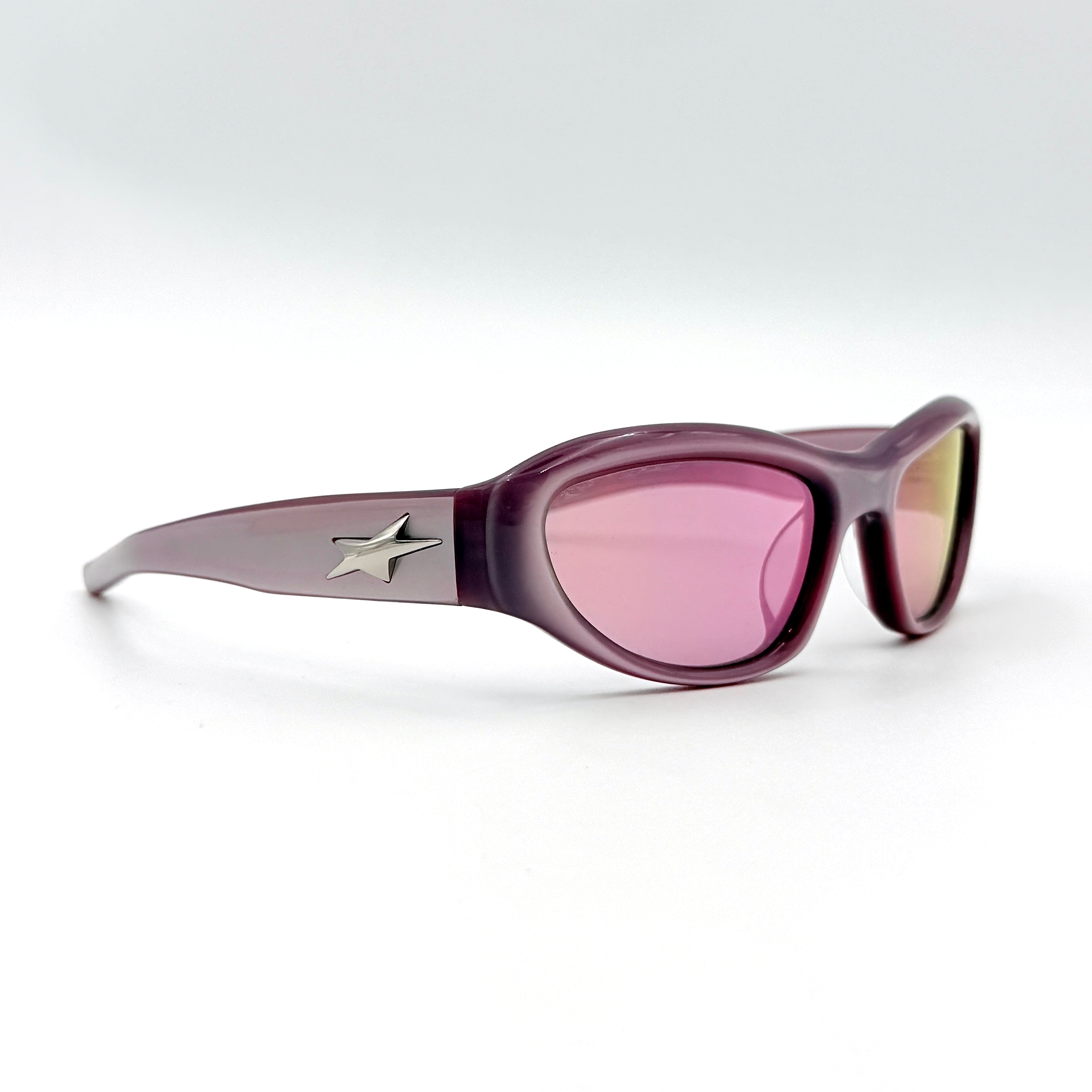 Gentle Monster R.E.A.T sunglasses in translucent pink acetate with mirrored pink lenses and silver star hardware, displayed alongside a chrome hard case.