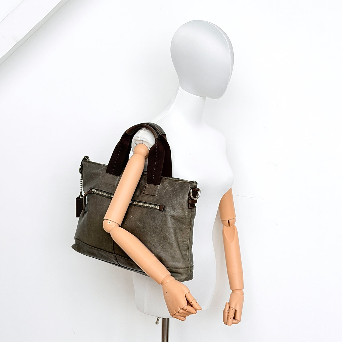 Coach brown leather tote bag with double handles and front zip pocket, shown on a white background.