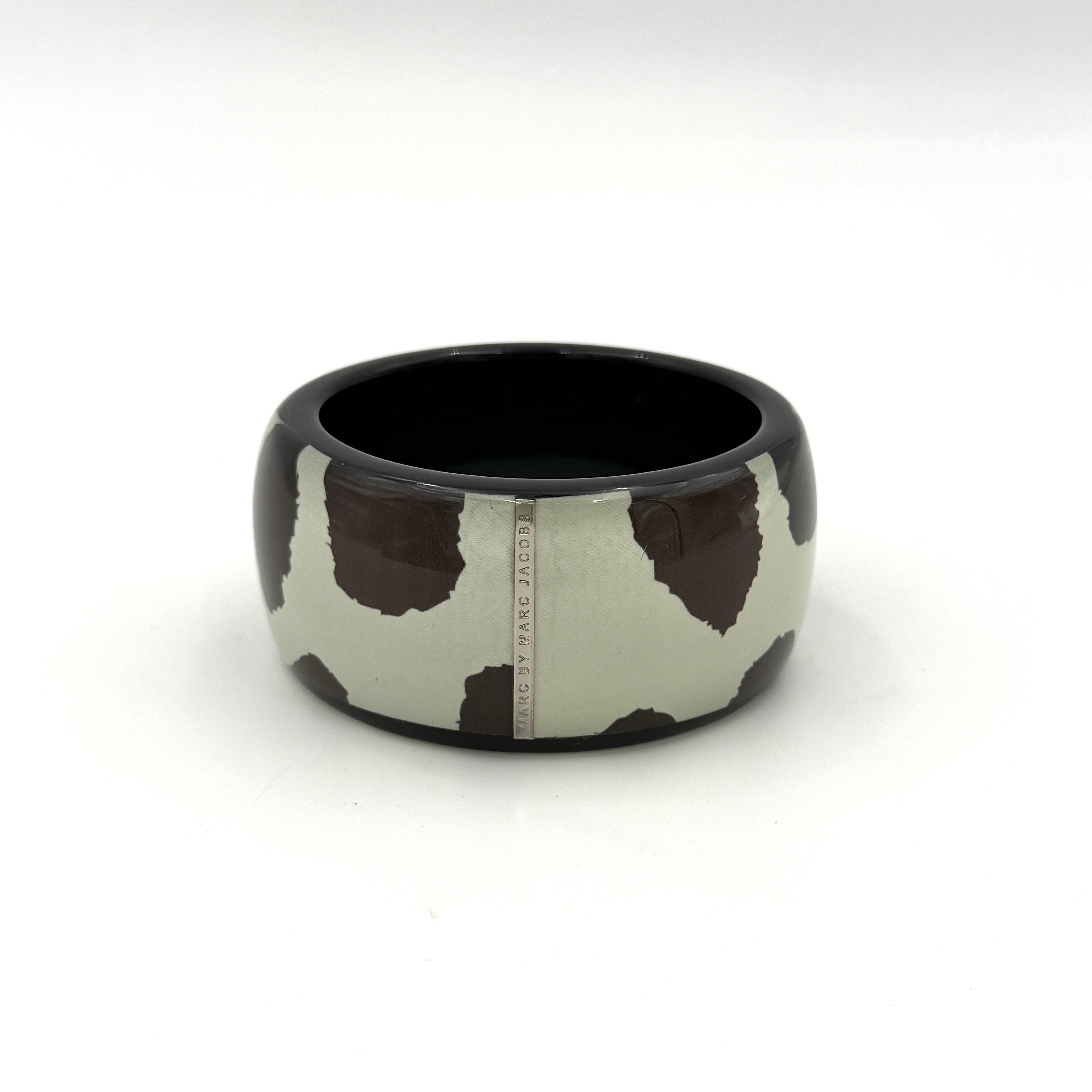A wide Marc Jacobs bangle bracelet in sage green and dark brown cow print resin, featuring a slim silvertone logo plaque.