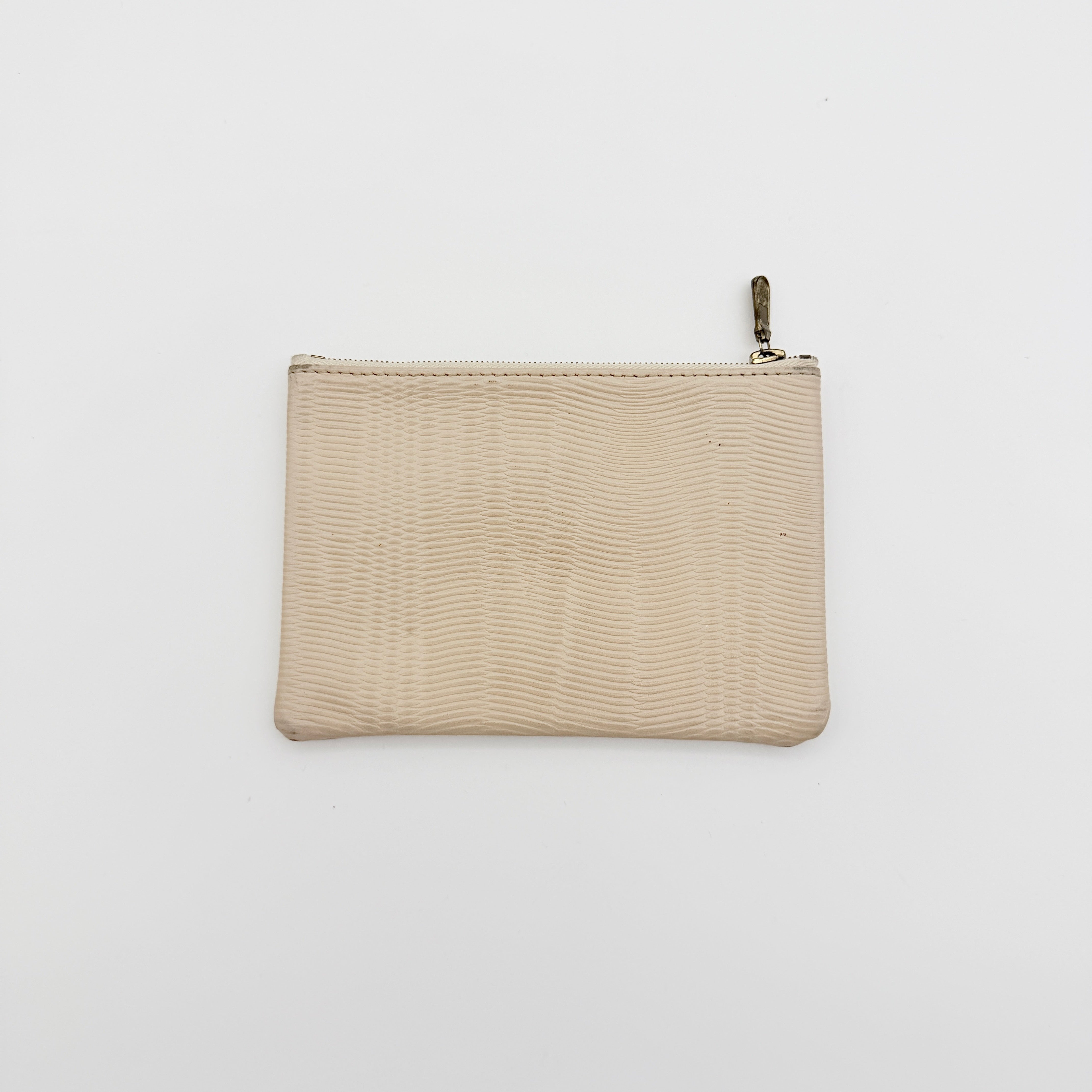 MCM beige embossed leather pouch with iconic gold logo plaque and zip closure, styled against a white background.