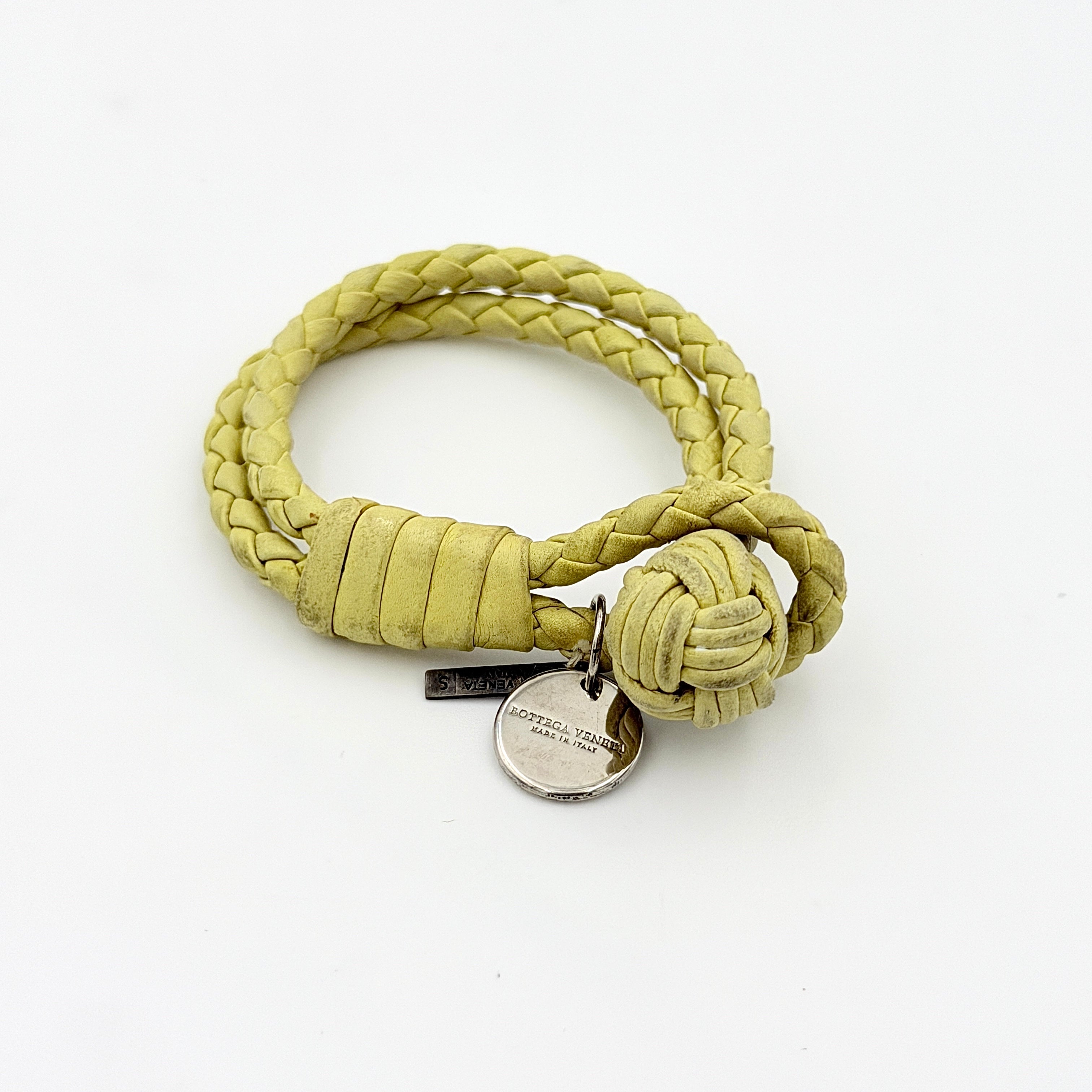 A braided pastel yellow Bottega Veneta Intrecciato leather bracelet with signature knot closure and engraved silver-tone tags.