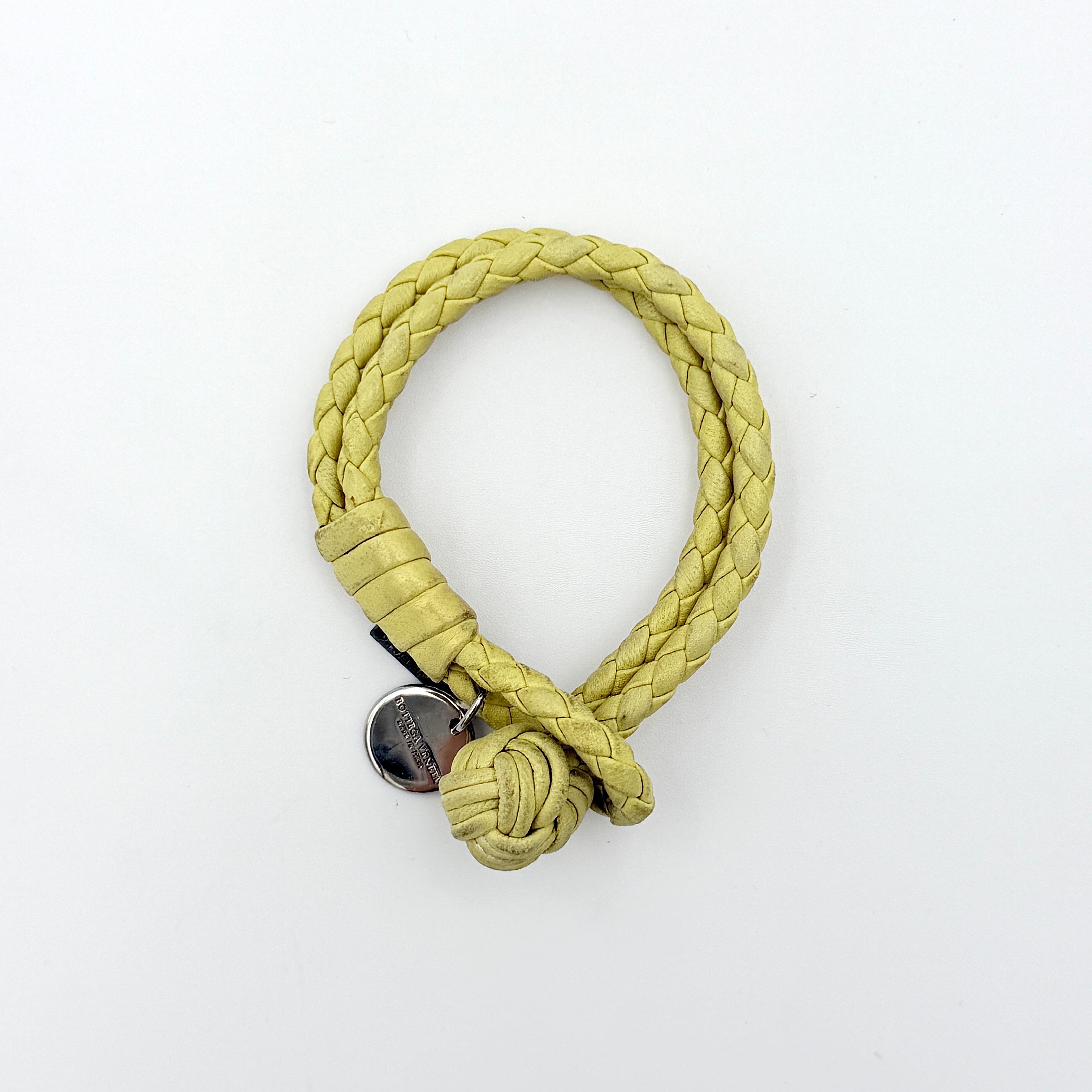 A braided pastel yellow Bottega Veneta Intrecciato leather bracelet with signature knot closure and engraved silver-tone tags.
