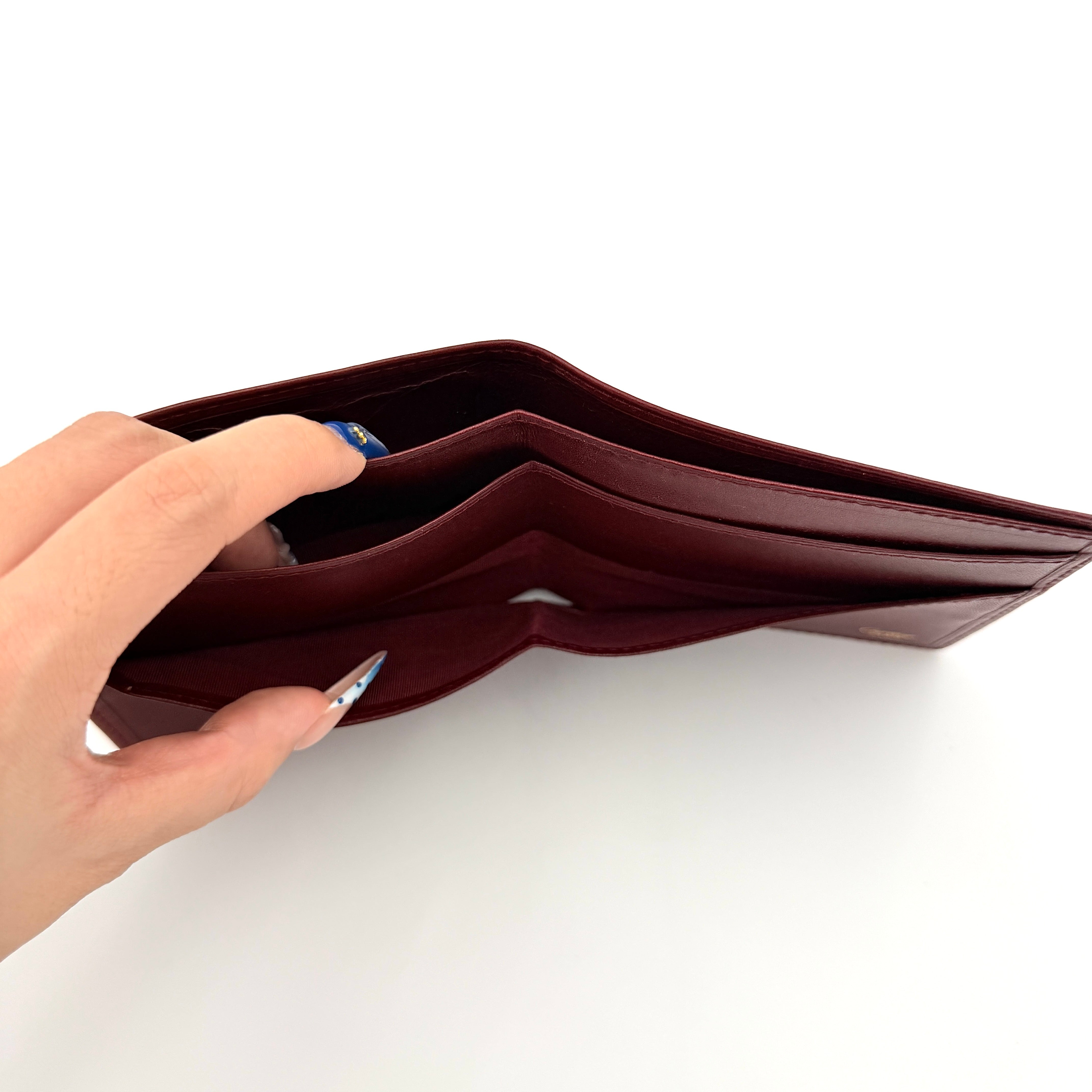 Cartier Must de Cartier leather wallet in rich burgundy with gold-tone corner accents and an embossed logo, photographed closed against a white background.