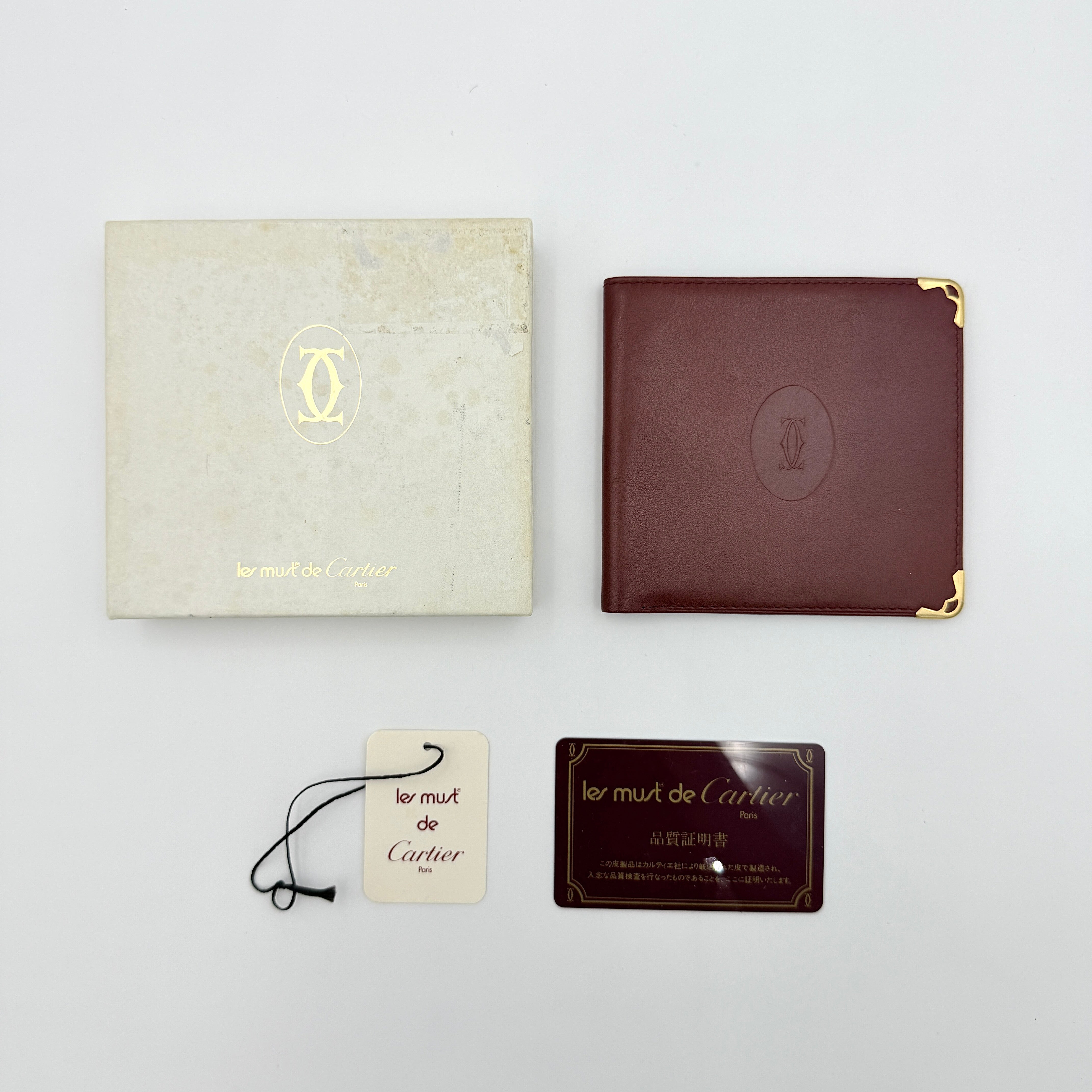 Cartier Must de Cartier leather wallet in rich burgundy with gold-tone corner accents and an embossed logo, photographed closed against a white background.