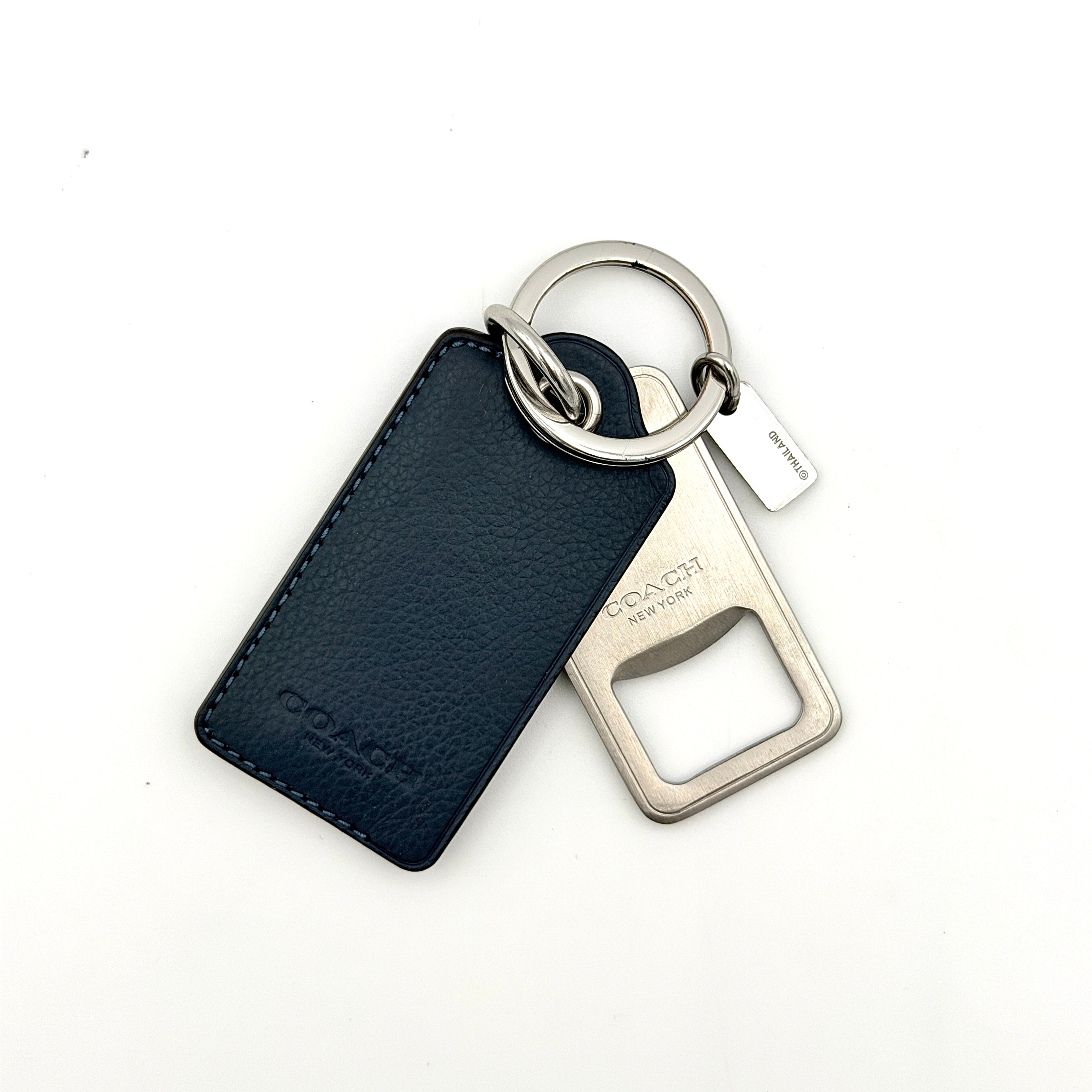 Coach bottle opener key fob in navy blue pebbled leather and silver-tone hardware, featuring a Coach New York embossed tag and integrated opener.