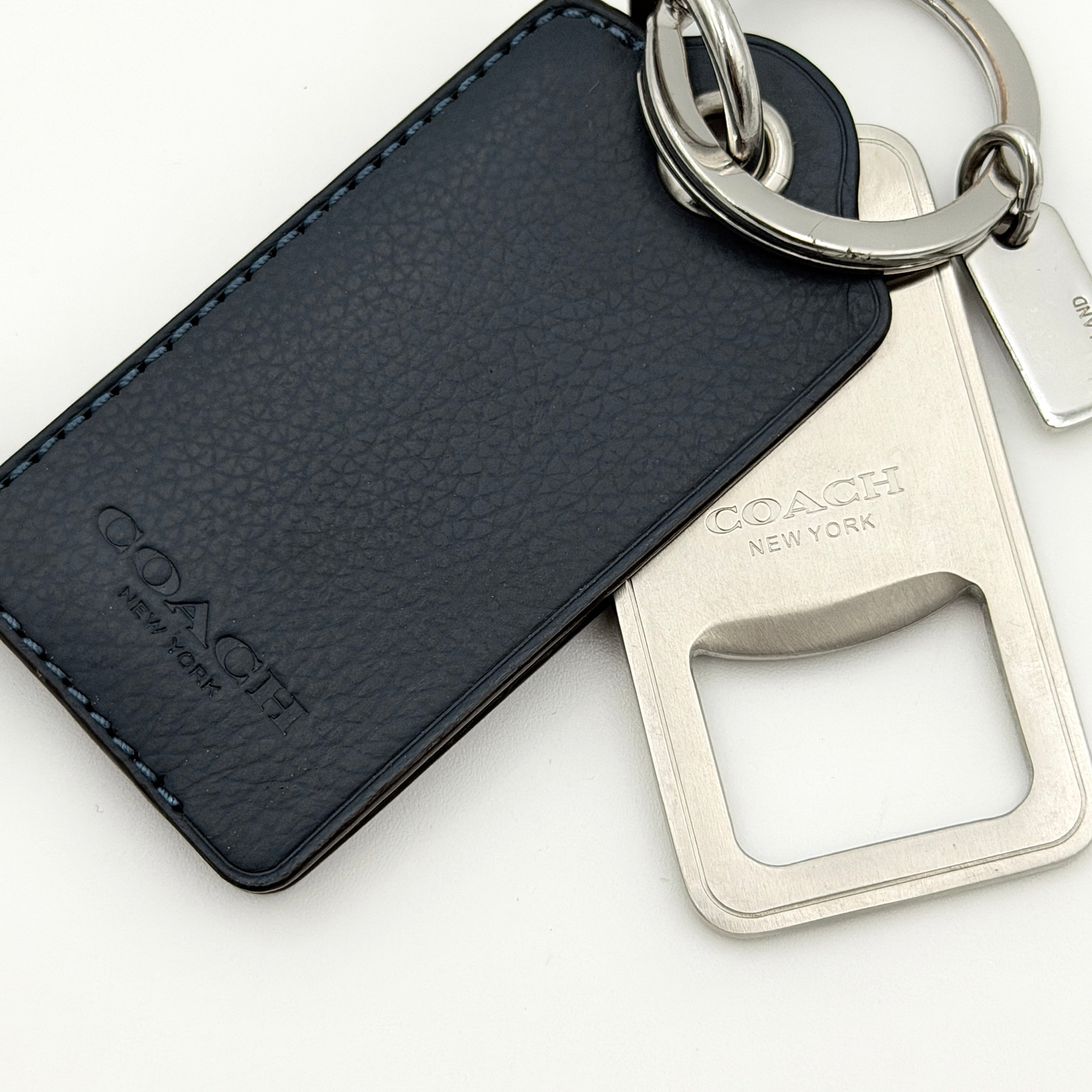 Coach bottle opener key fob in navy blue pebbled leather and silver-tone hardware, featuring a Coach New York embossed tag and integrated opener.