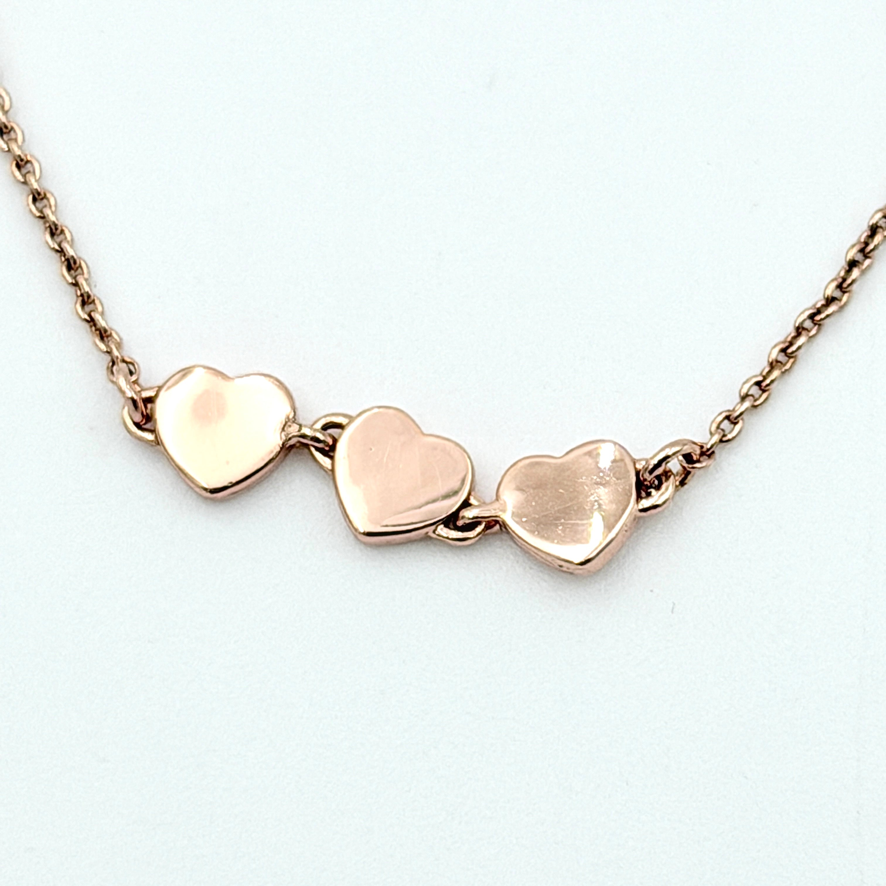 Coach gold bracelet featuring three heart-shaped charms, one with a crystal, one plain, and one engraved with the Coach logo.