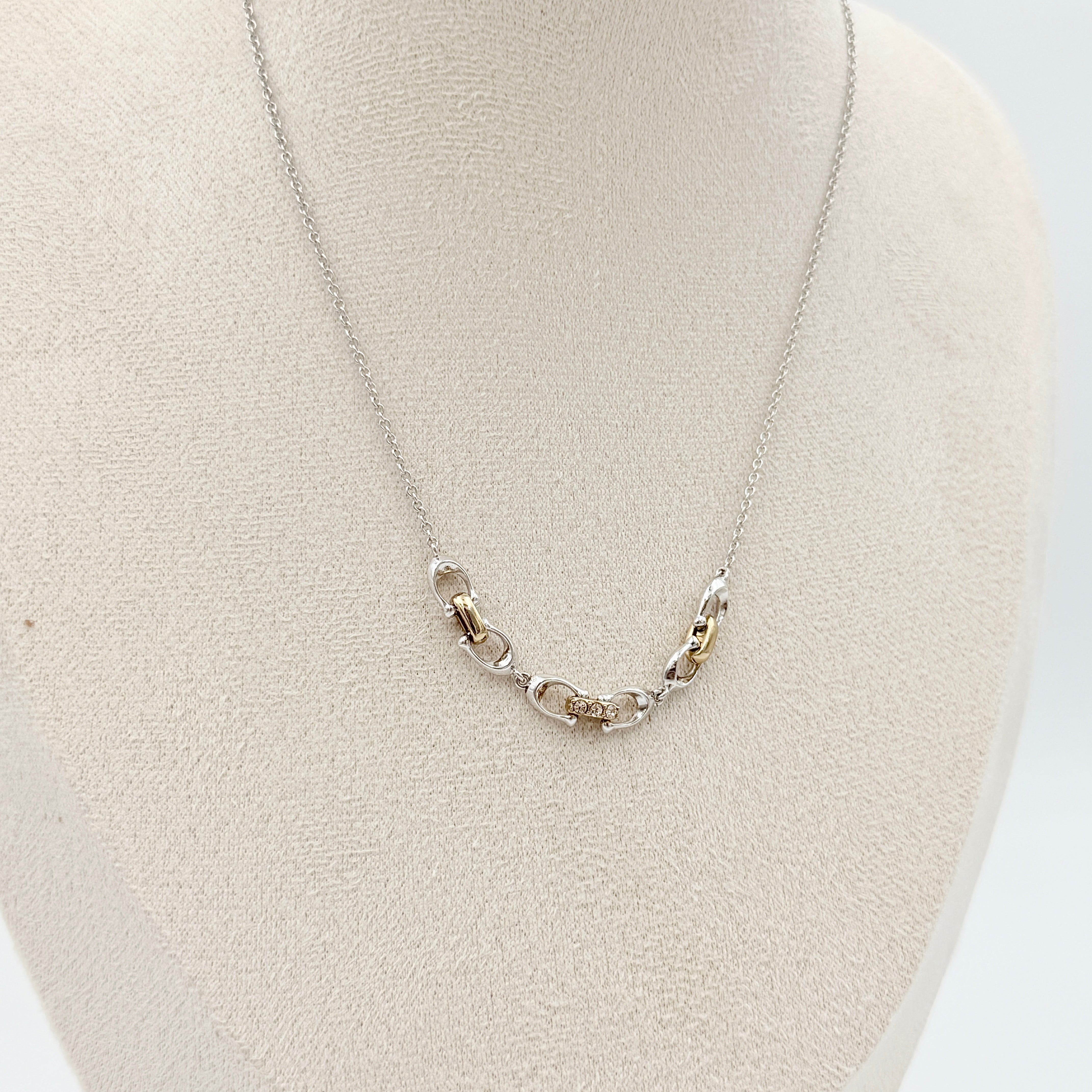 Coach Signature Linked Necklace in silver and gold tones featuring sculptural mixed-metal links and a central crystal accent.