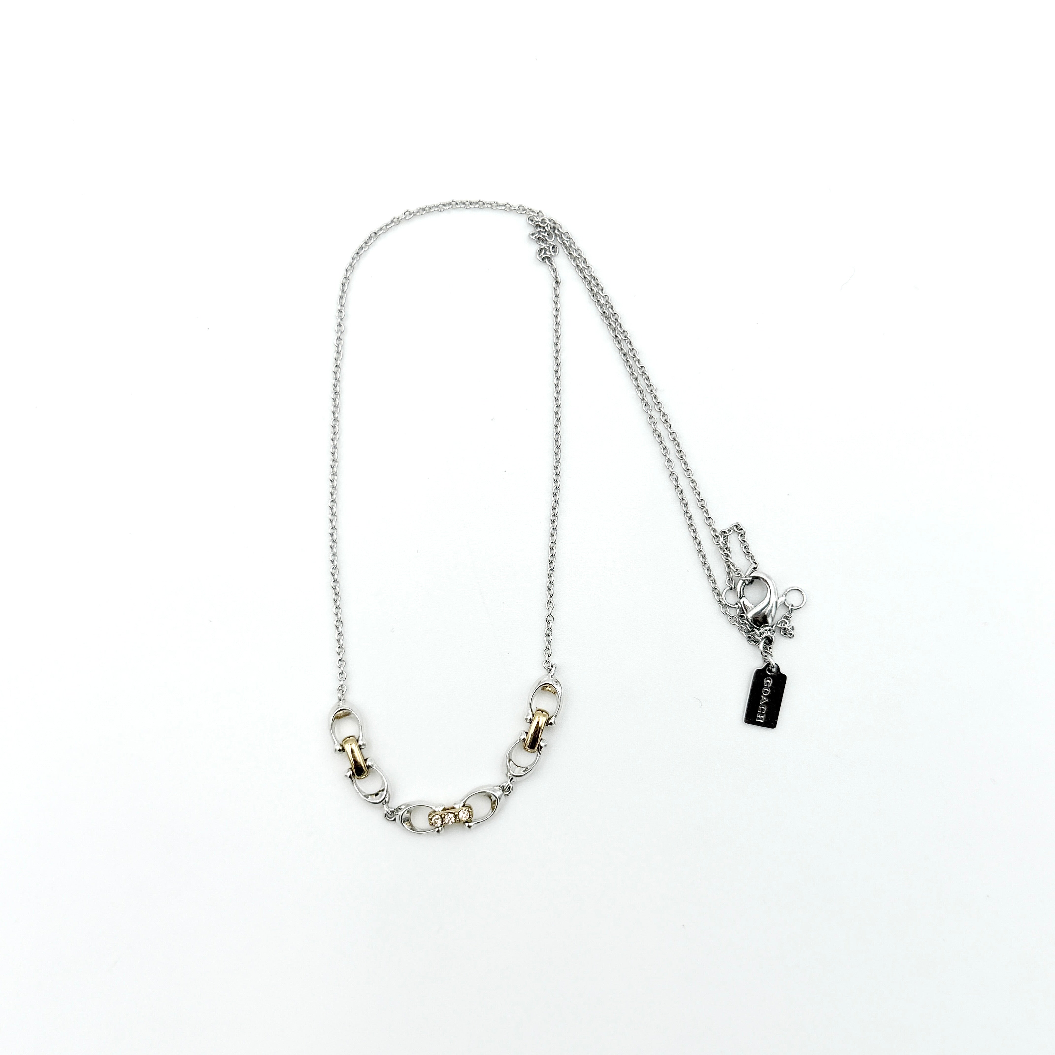 Coach Signature Linked Necklace in silver and gold tones featuring sculptural mixed-metal links and a central crystal accent.