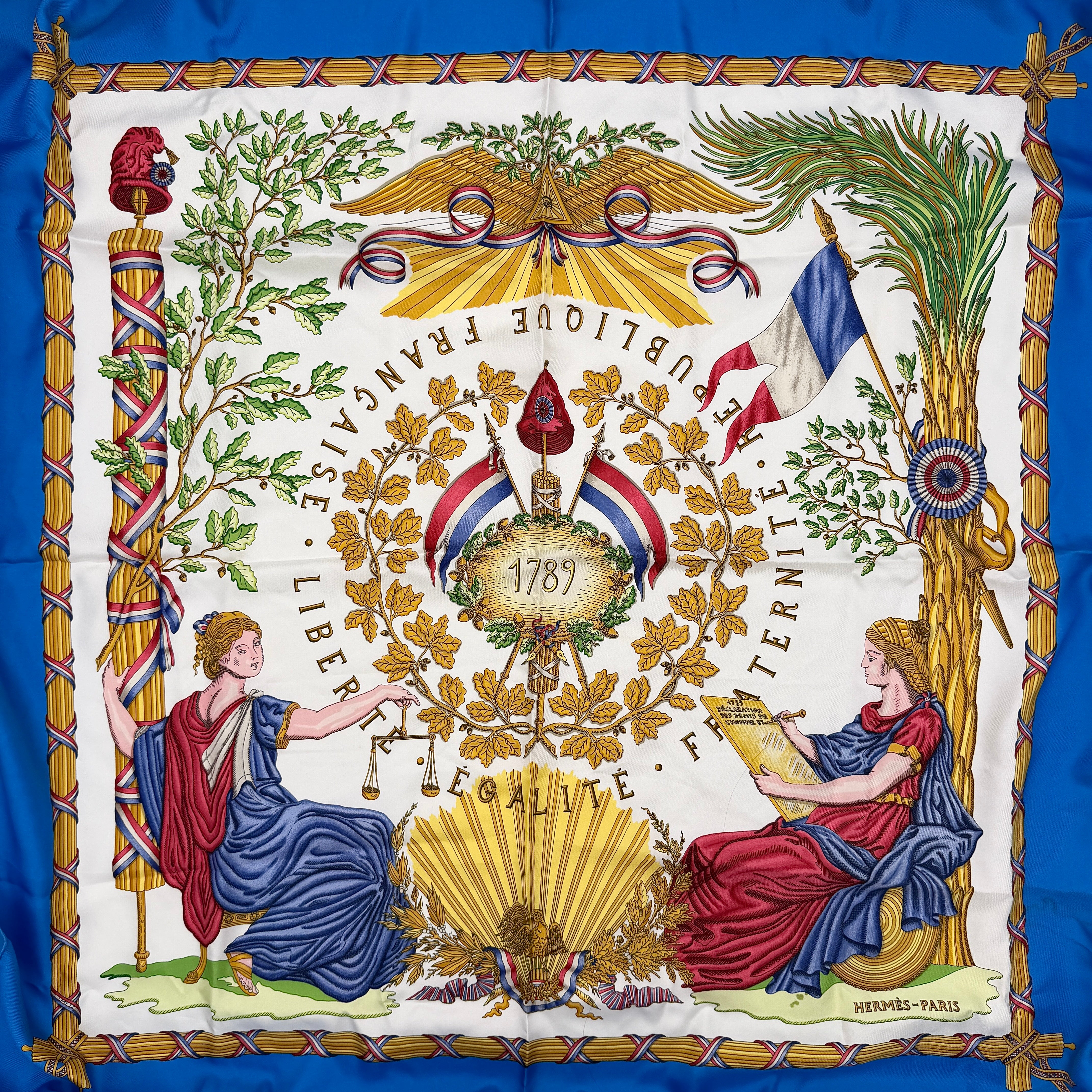 Hermès silk scarf with blue border, featuring a detailed French revolutionary motif and classical figures, shown with its signature orange box.