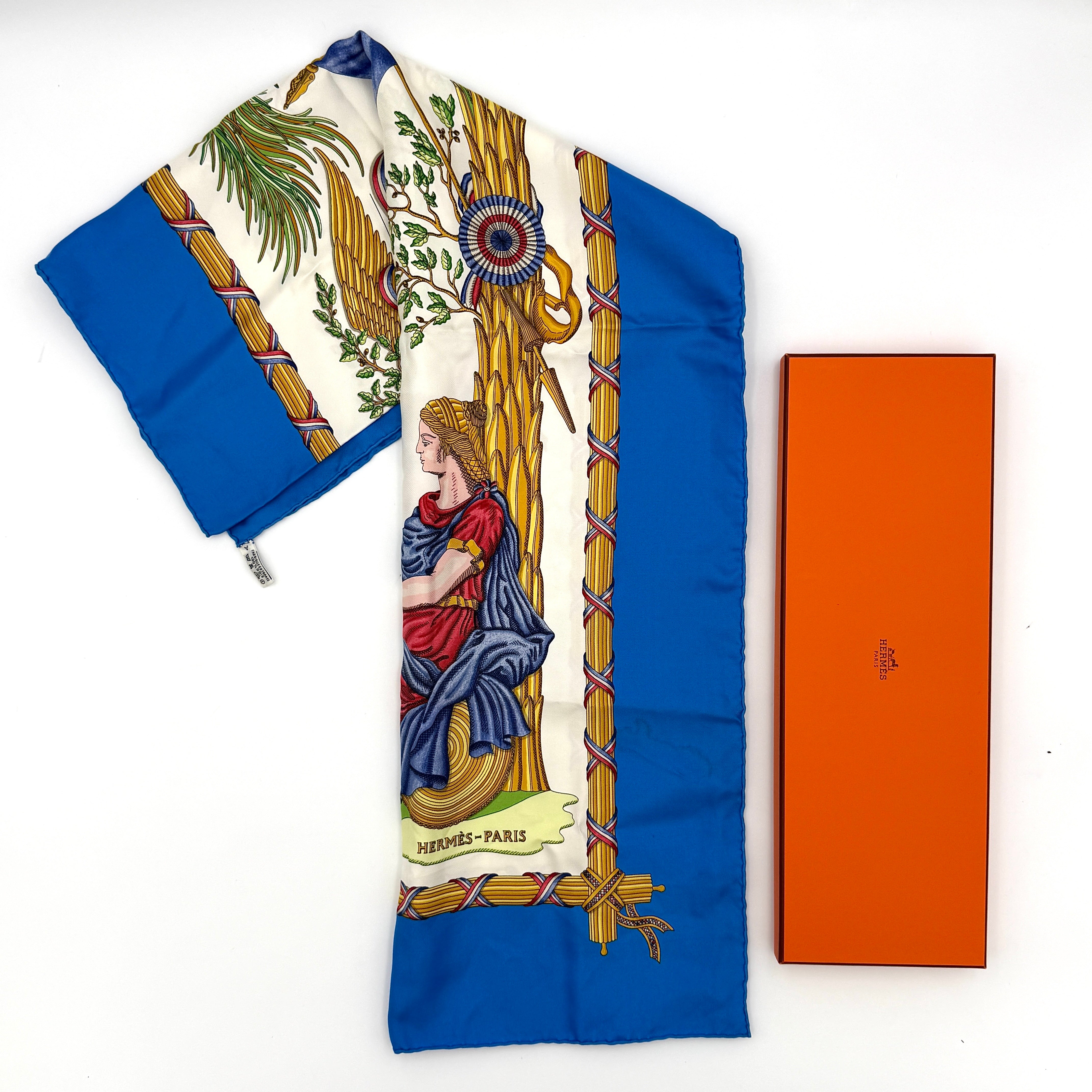 Hermès silk scarf with blue border, featuring a detailed French revolutionary motif and classical figures, shown with its signature orange box.