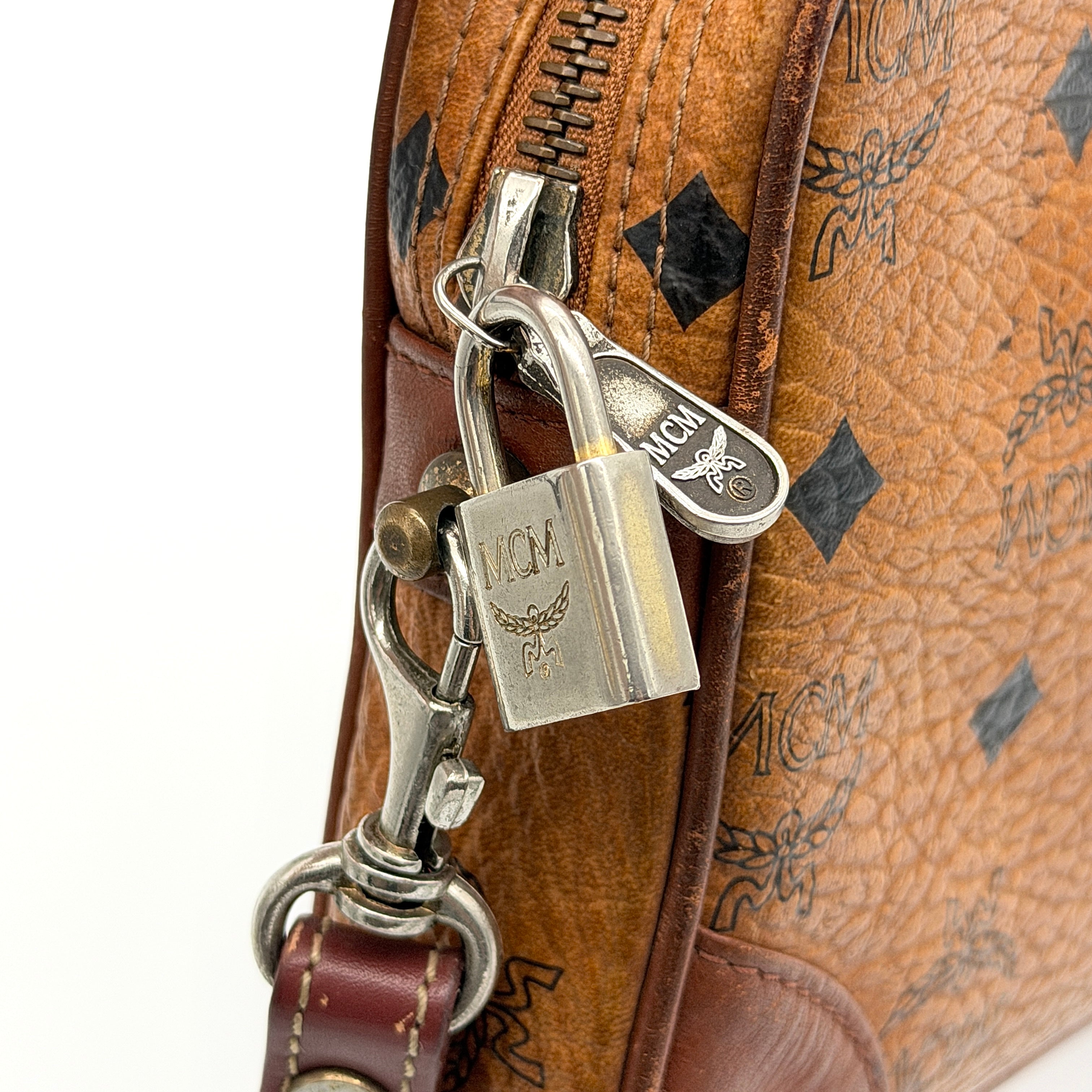 MCM Visetos monogram clutch bag in brown coated canvas with wristlet strap and gold logo plaque, photographed on white background.