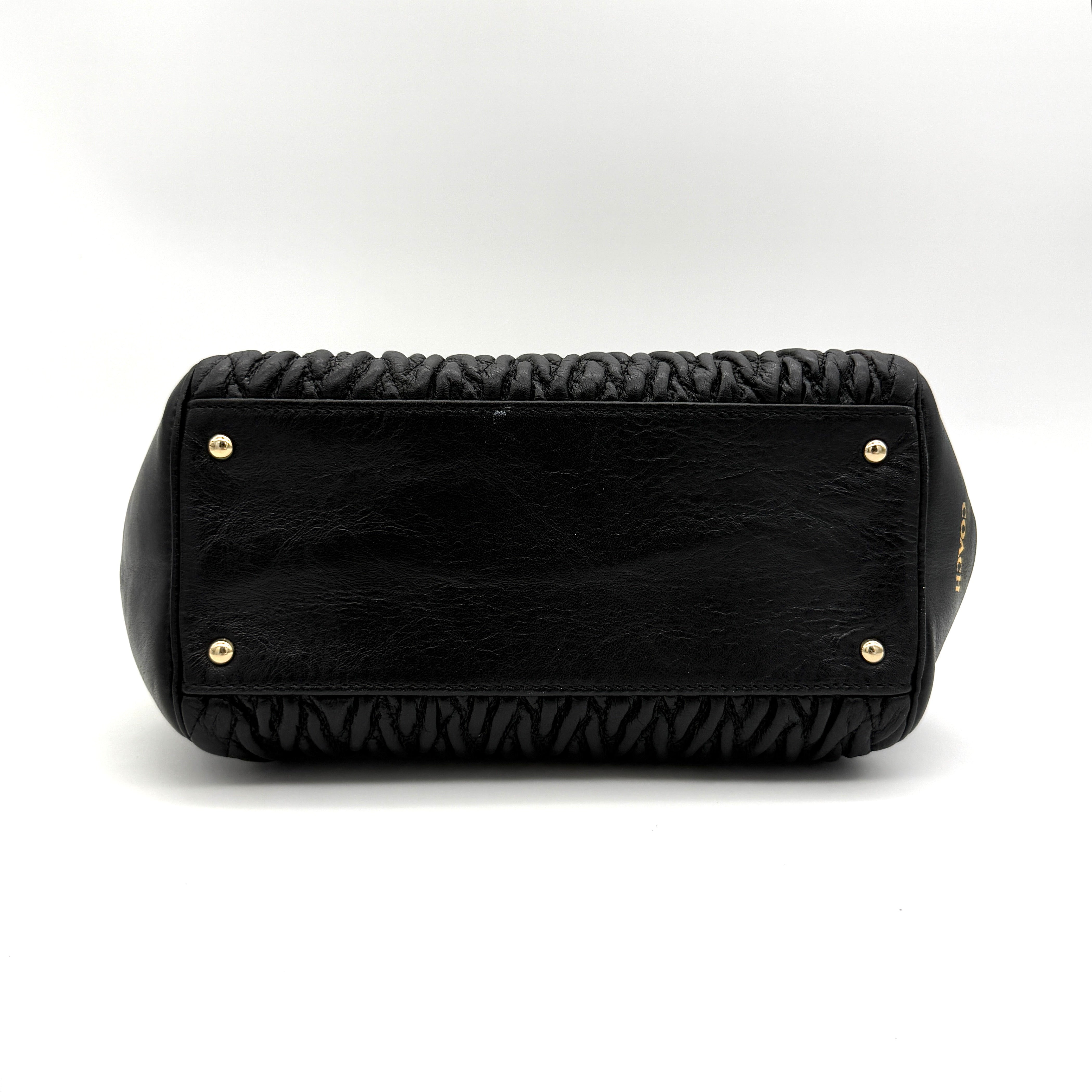 Coach Madison Gathered Twist satchel in black leather with gold hardware and detachable strap, styled on a white background.