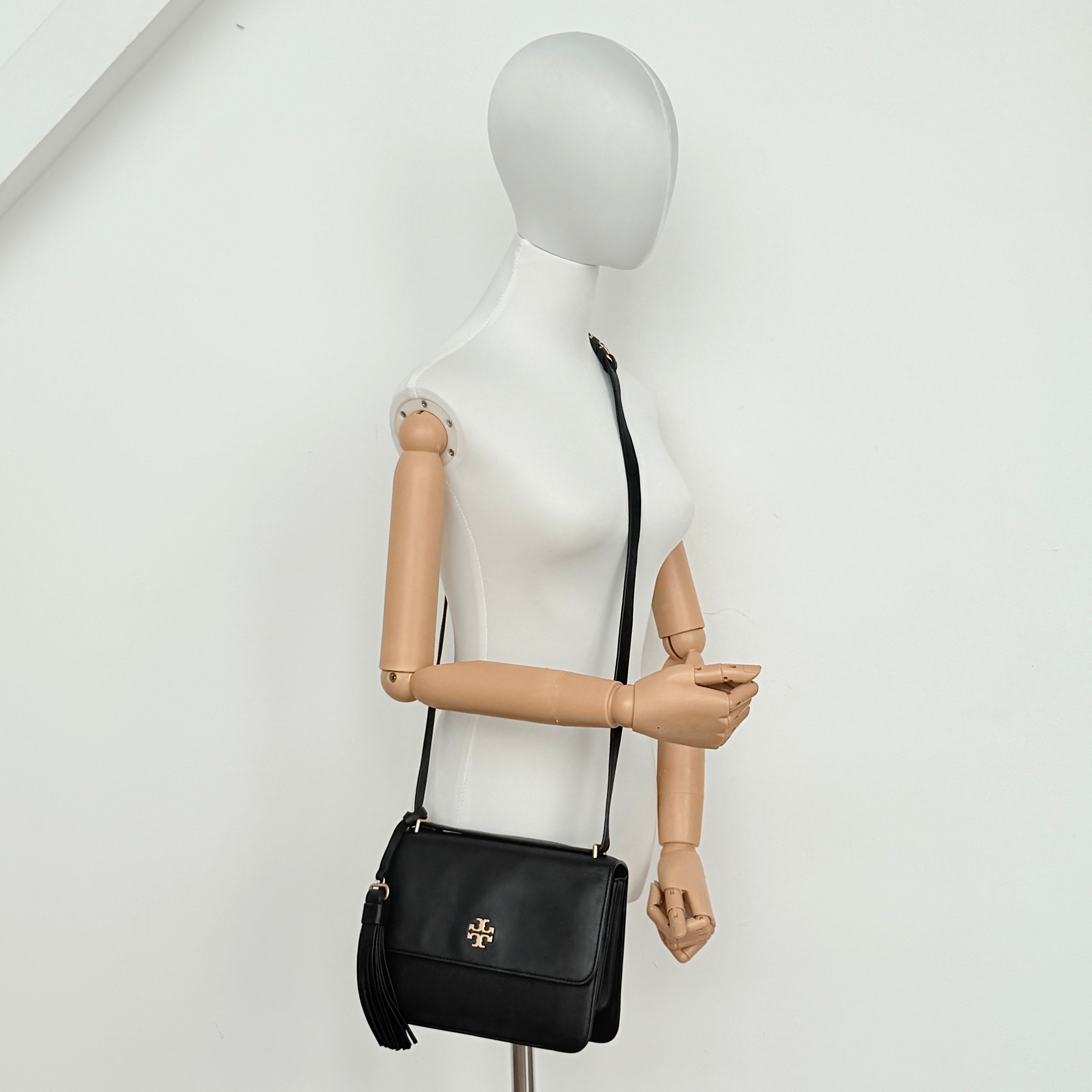 Tory Burch Brooke Crossbody Bag in black leather with gold-tone logo and a braided chain strap, elegantly displayed against a white backdrop.