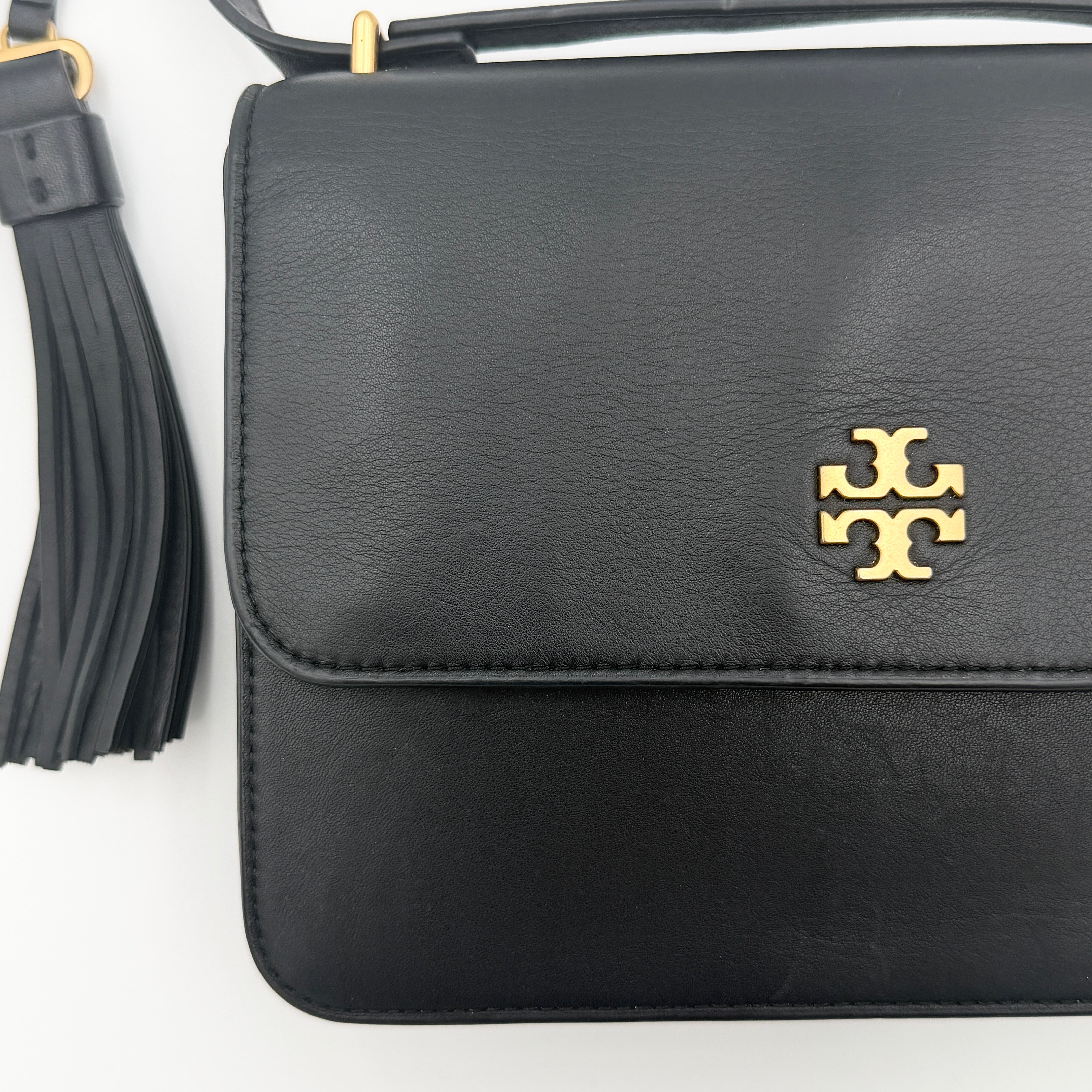 Tory Burch Brooke Crossbody Bag in black leather with gold-tone logo and a braided chain strap, elegantly displayed against a white backdrop.