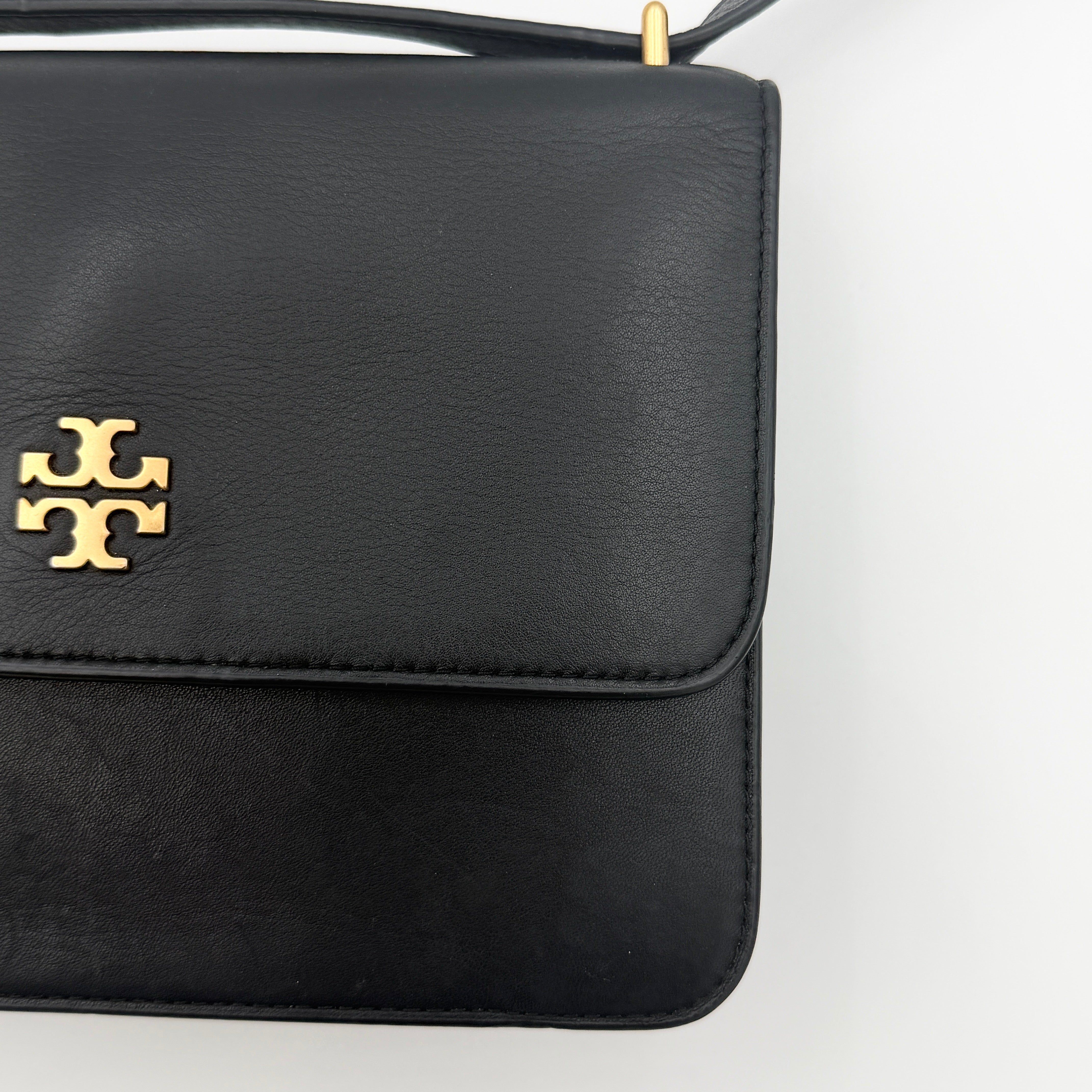 Tory Burch Brooke Crossbody Bag in black leather with gold-tone logo and a braided chain strap, elegantly displayed against a white backdrop.